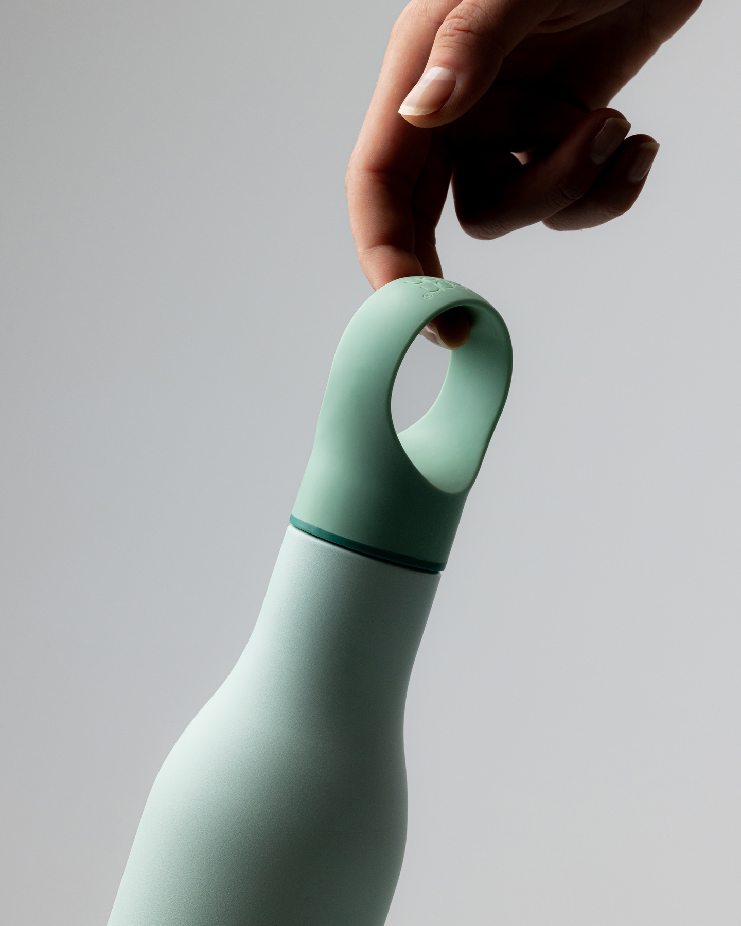 Hand holding a green water bottle by its flexible silicone loop cap