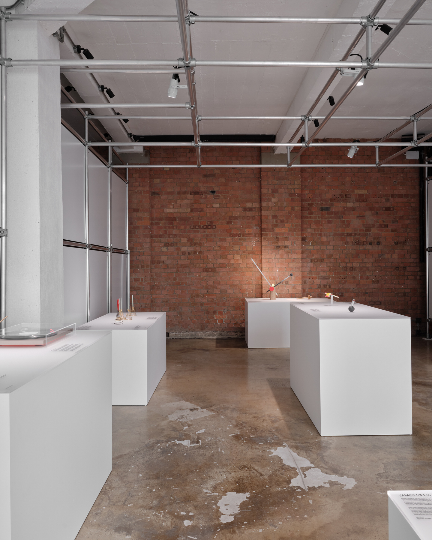 View down central gallery room with white plinths and exposed brick wall