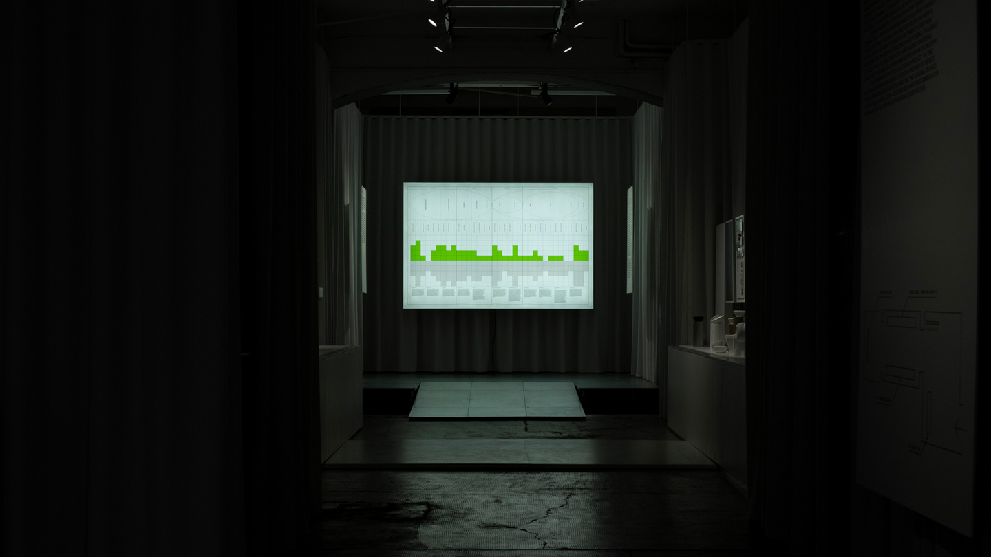 View through an doorway leading to a lit presentation screen in a dark gallery