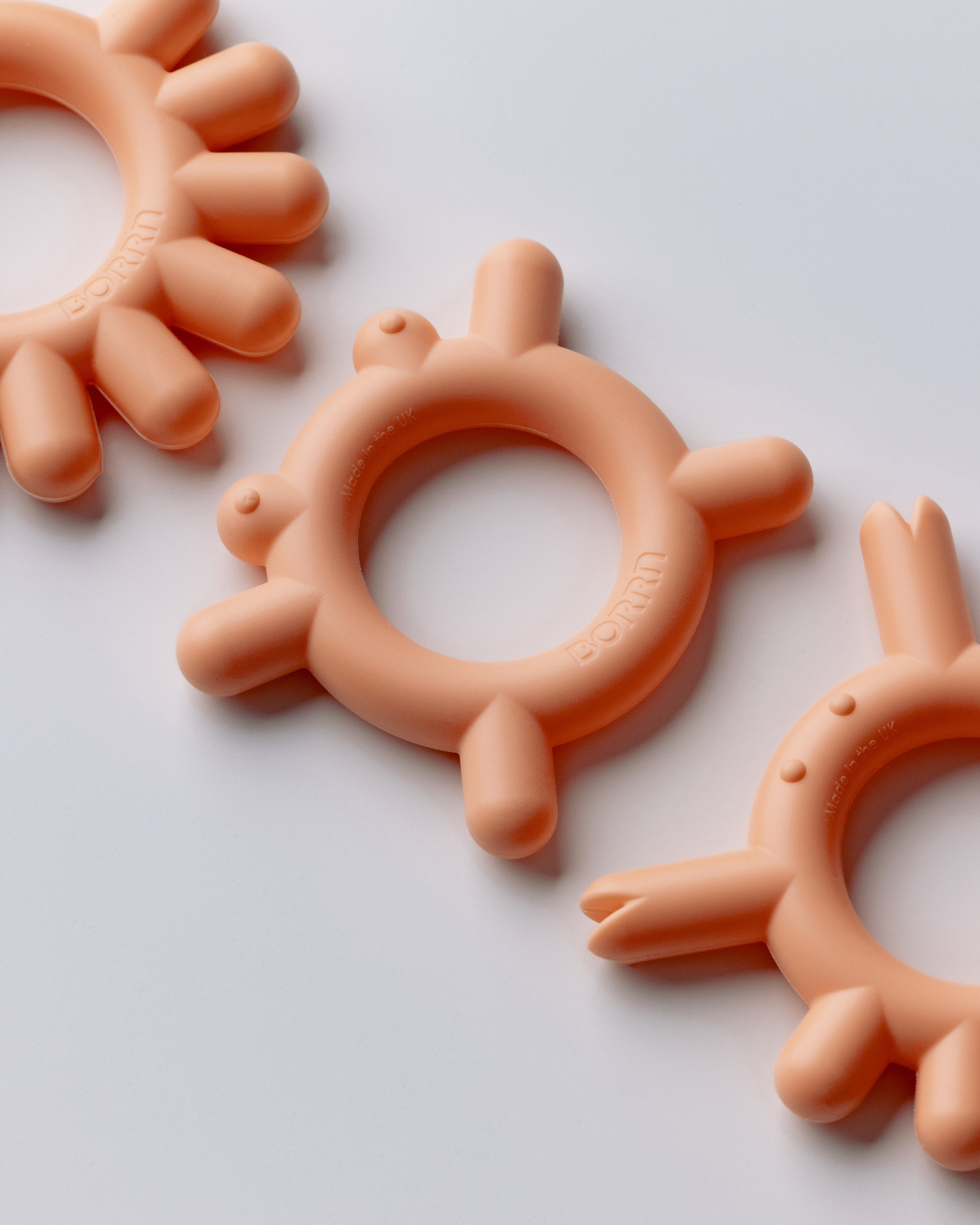 Peach-coloured teethers in a line-up on a light background.