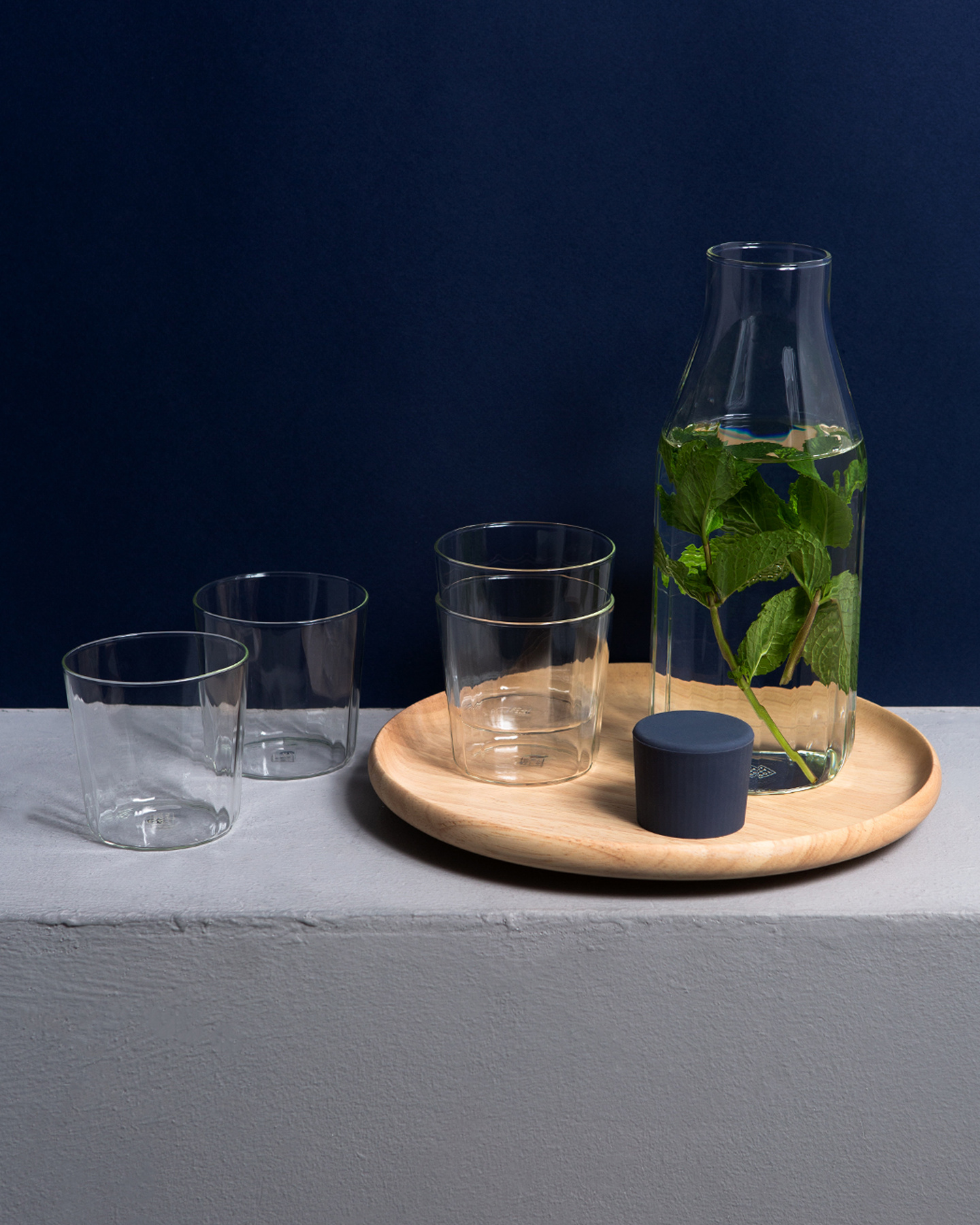 Clear glass bottle and tumblers set on a round wooden tray with dark background