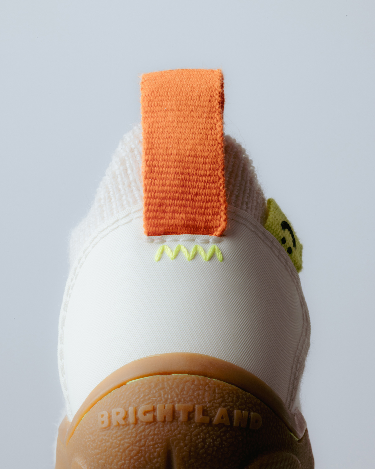 Close-up top view of a white shoe heel pull tab with orange detail.