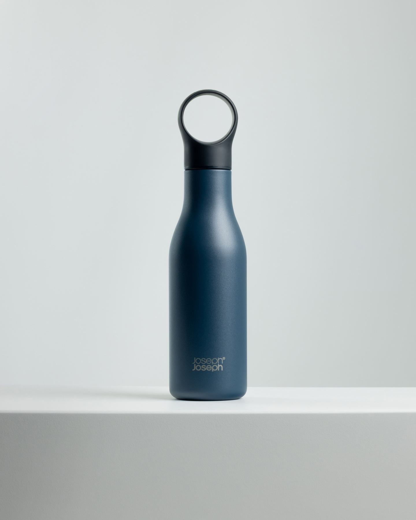 Dark blue water bottle with loop lid standing on a white surface