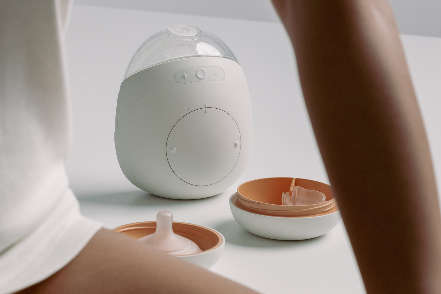 Seated woman with the Avira breast pump resting on a surface in the background.