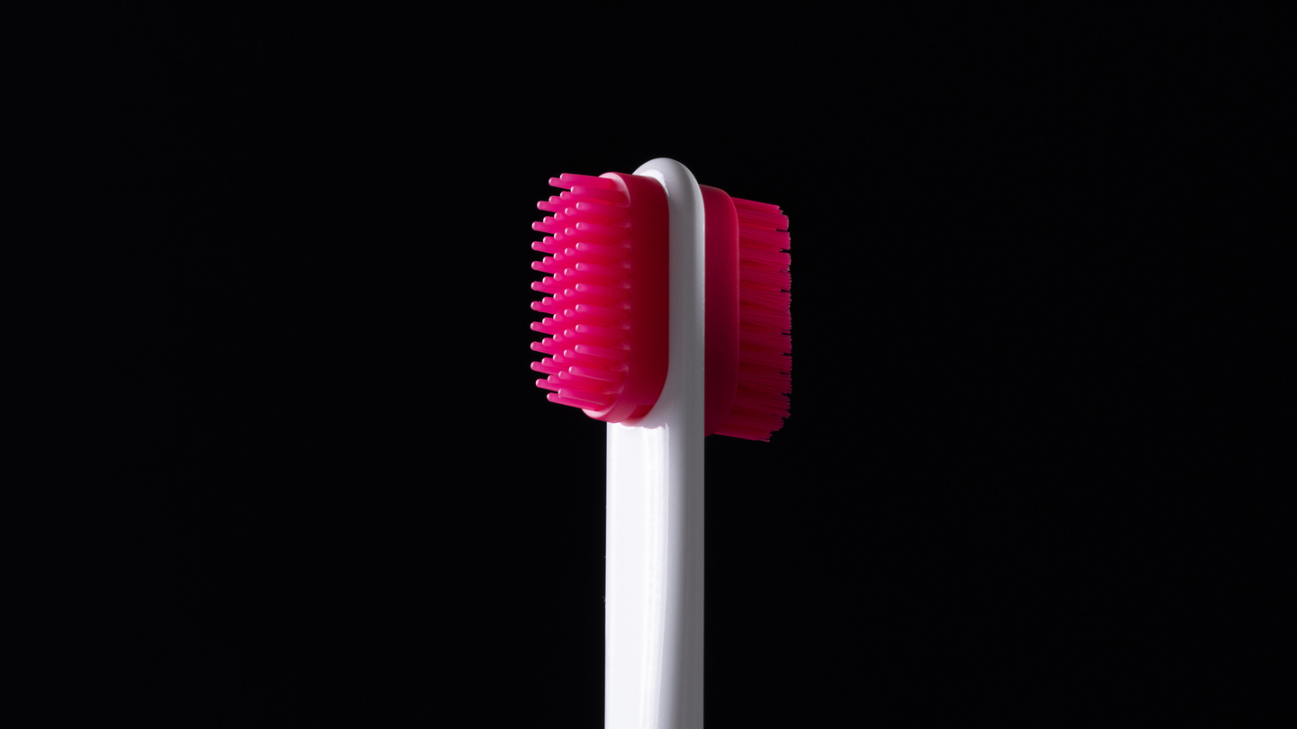 Bright pink double-sided bristle brush attachment on a dark background