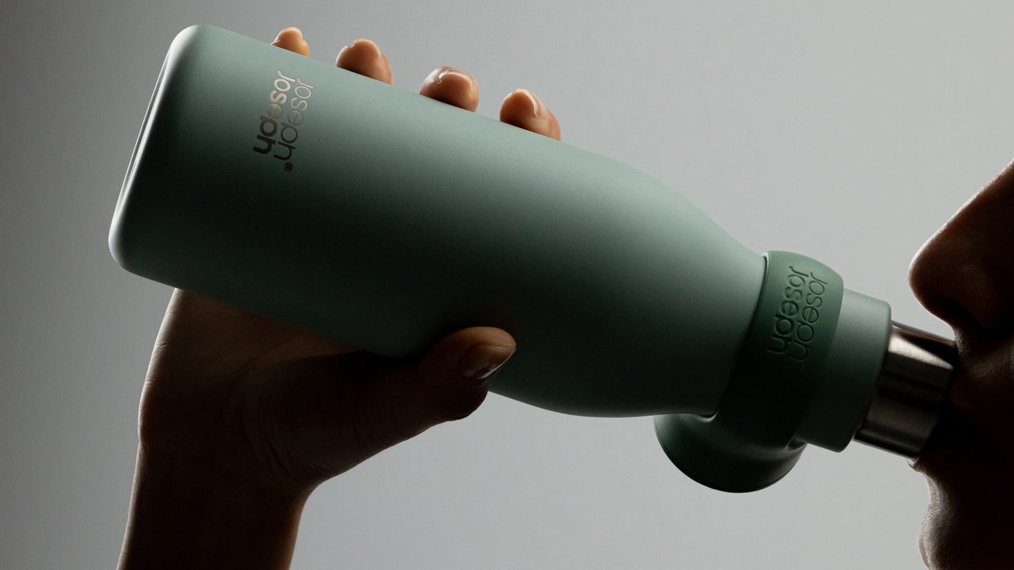 Hands holding a green water bottle horizontally against a dark background