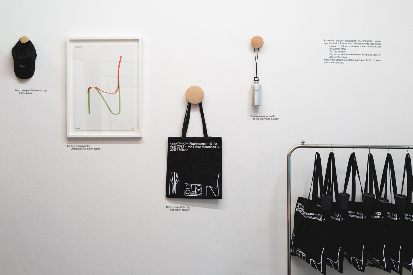 A white wall displays a framed graphic print, merchandise of the exhibition and a rack of black tote bags.