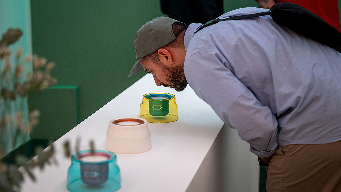 Visitor wearing a cap leaning over a low display table to inspect design objects.