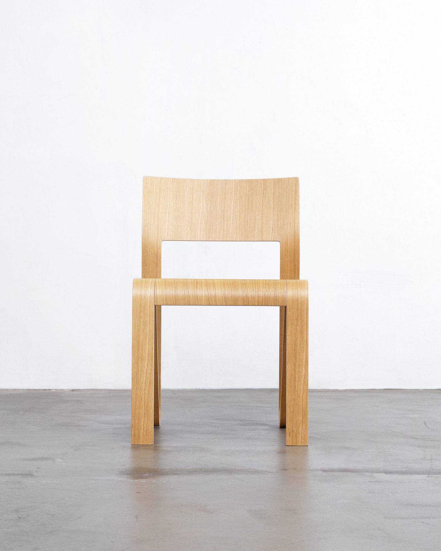 Front view of a light wooden chair with a minimal plywood frame standing on a concrete floor.