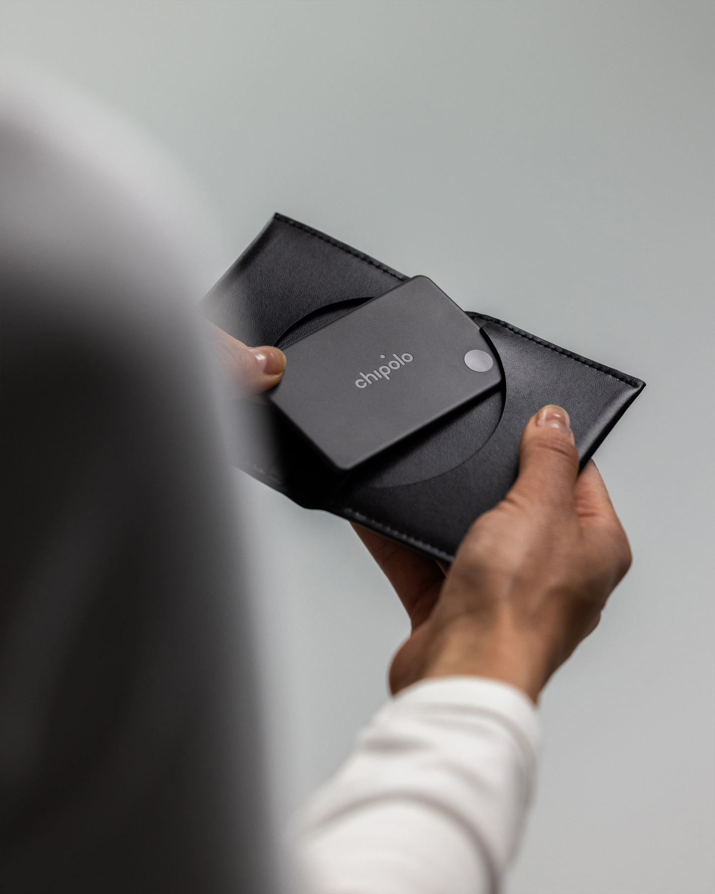 Hands inserting a black rectangular Chipolo Card tracker into a leather wallet.