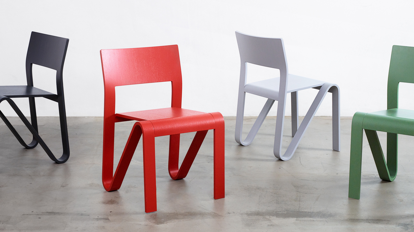 Lineup of Peel Chairs in black, red, grey and green finishes on a studio floor.