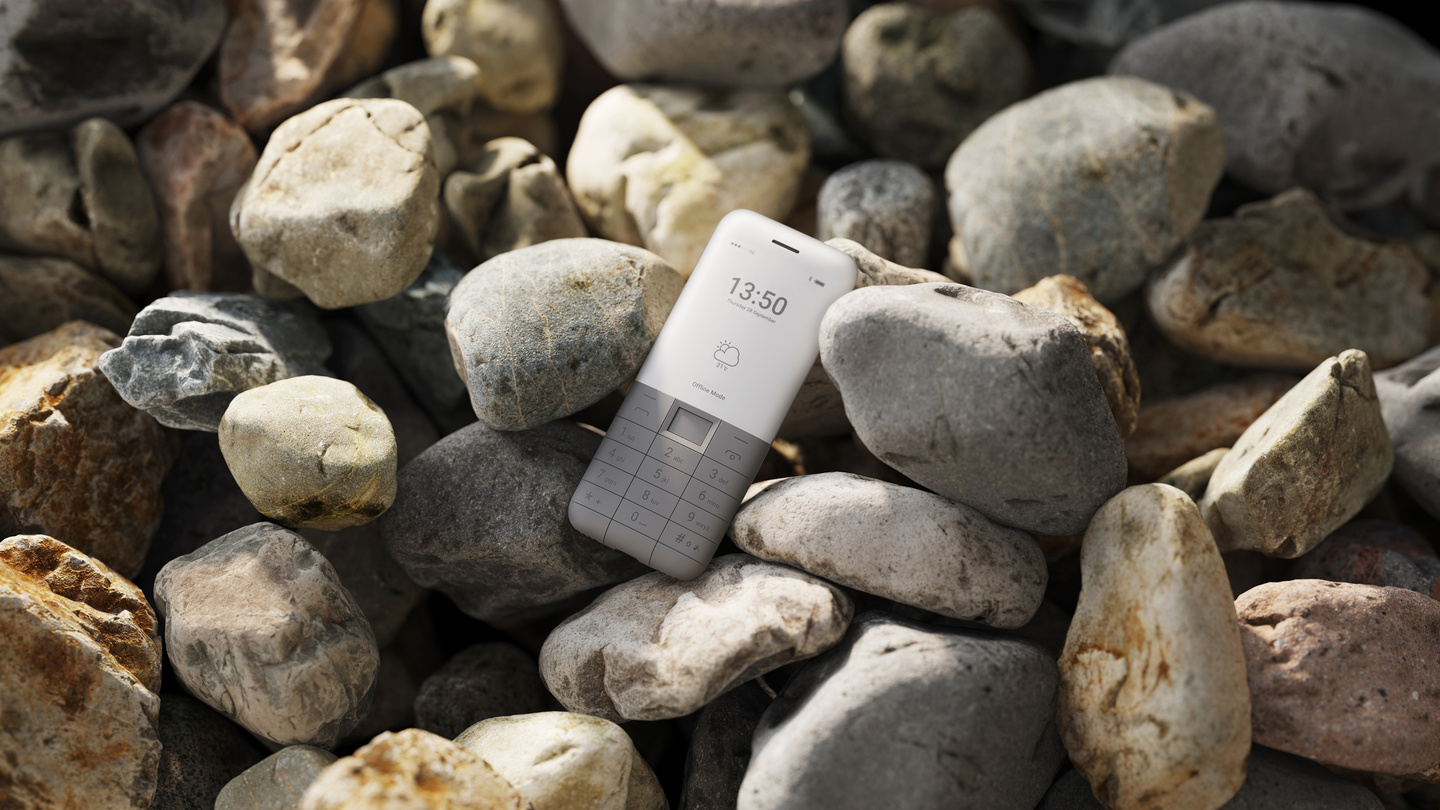 White minimalist keypad phone resting among smooth grey stones.