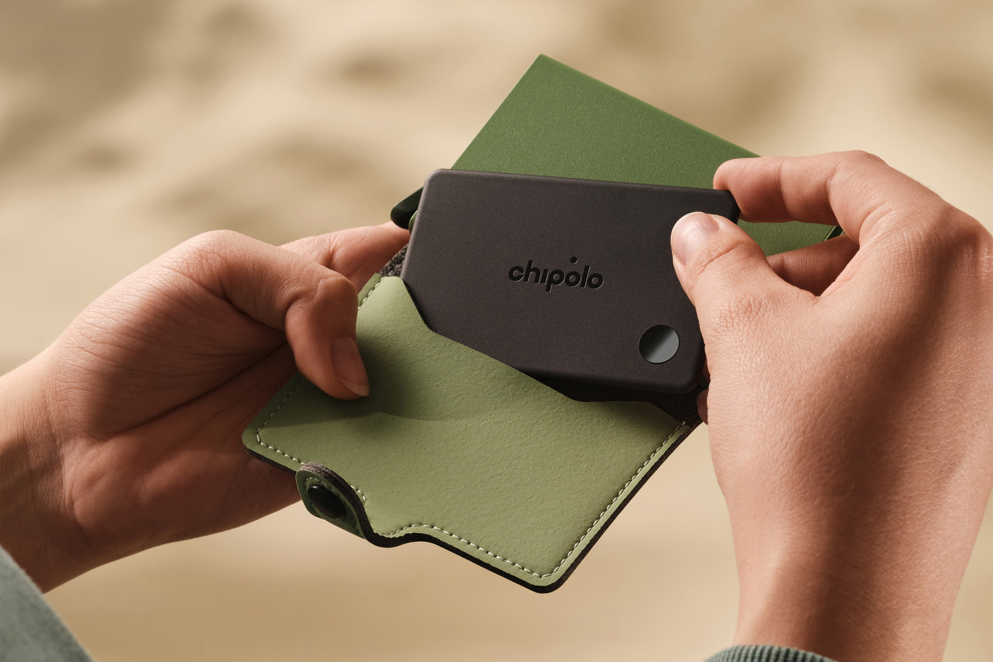 Close-up of hands inserting a black tracker card into a green leather case.