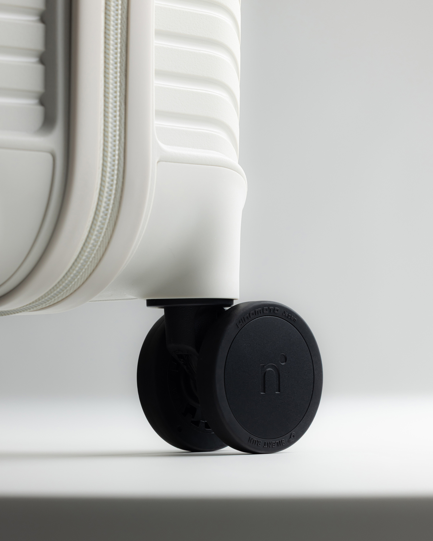 Single black caster wheel mounted on a white hardshell suitcase base