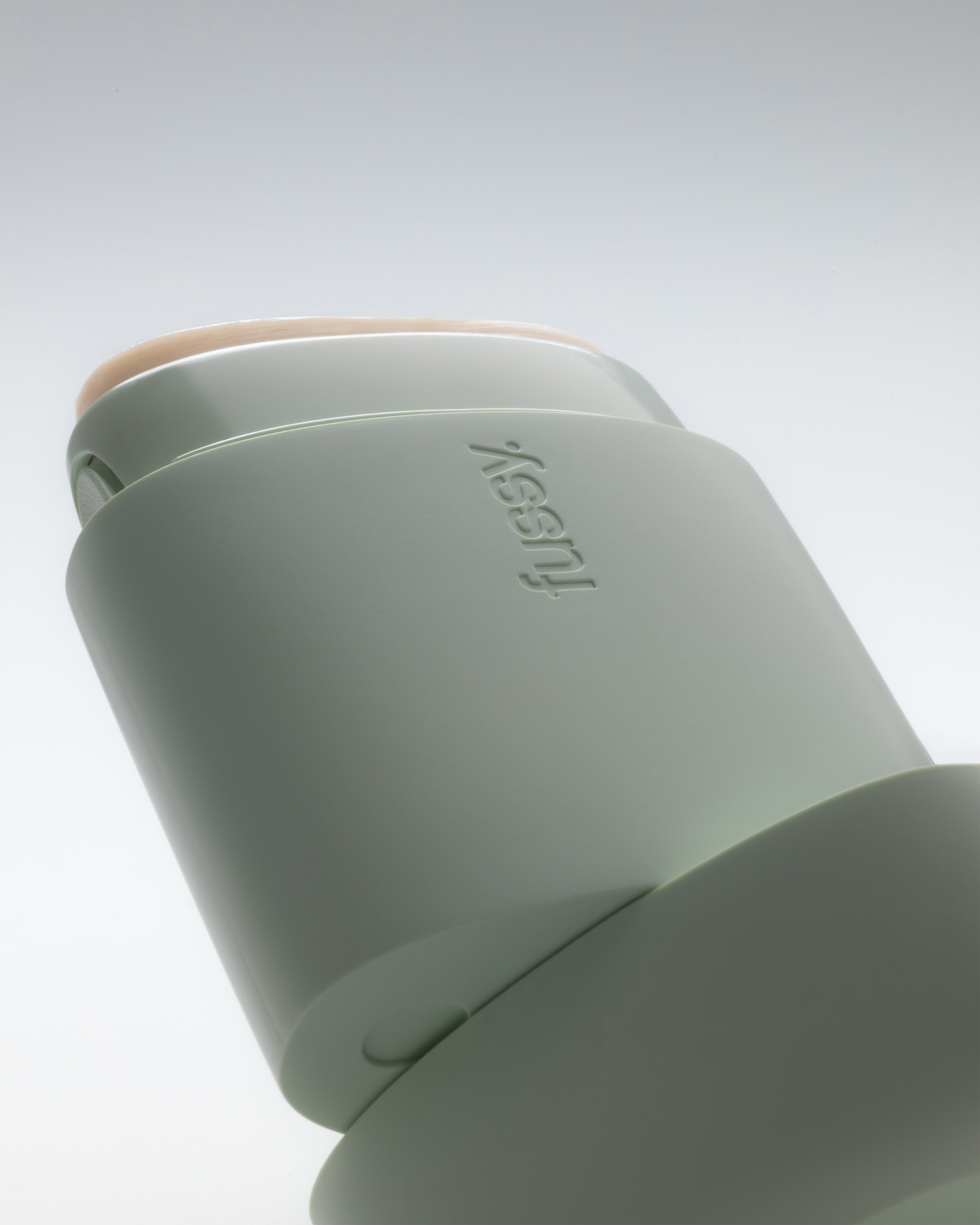 Low angle studio view of a mint green Fussy deodorant case on a plain background.
