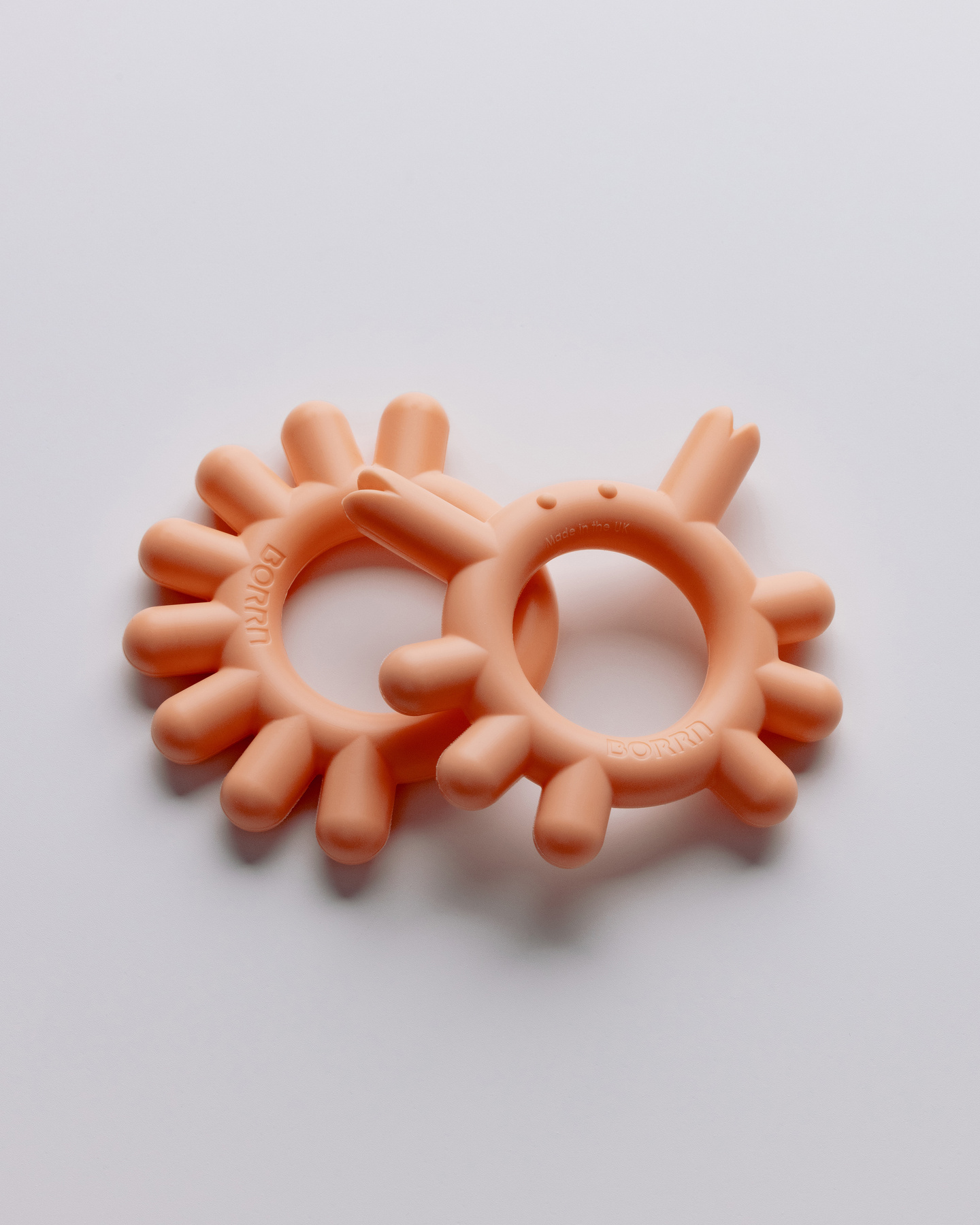 Top-down view of two peach-coloured silicone teethers on a light background.