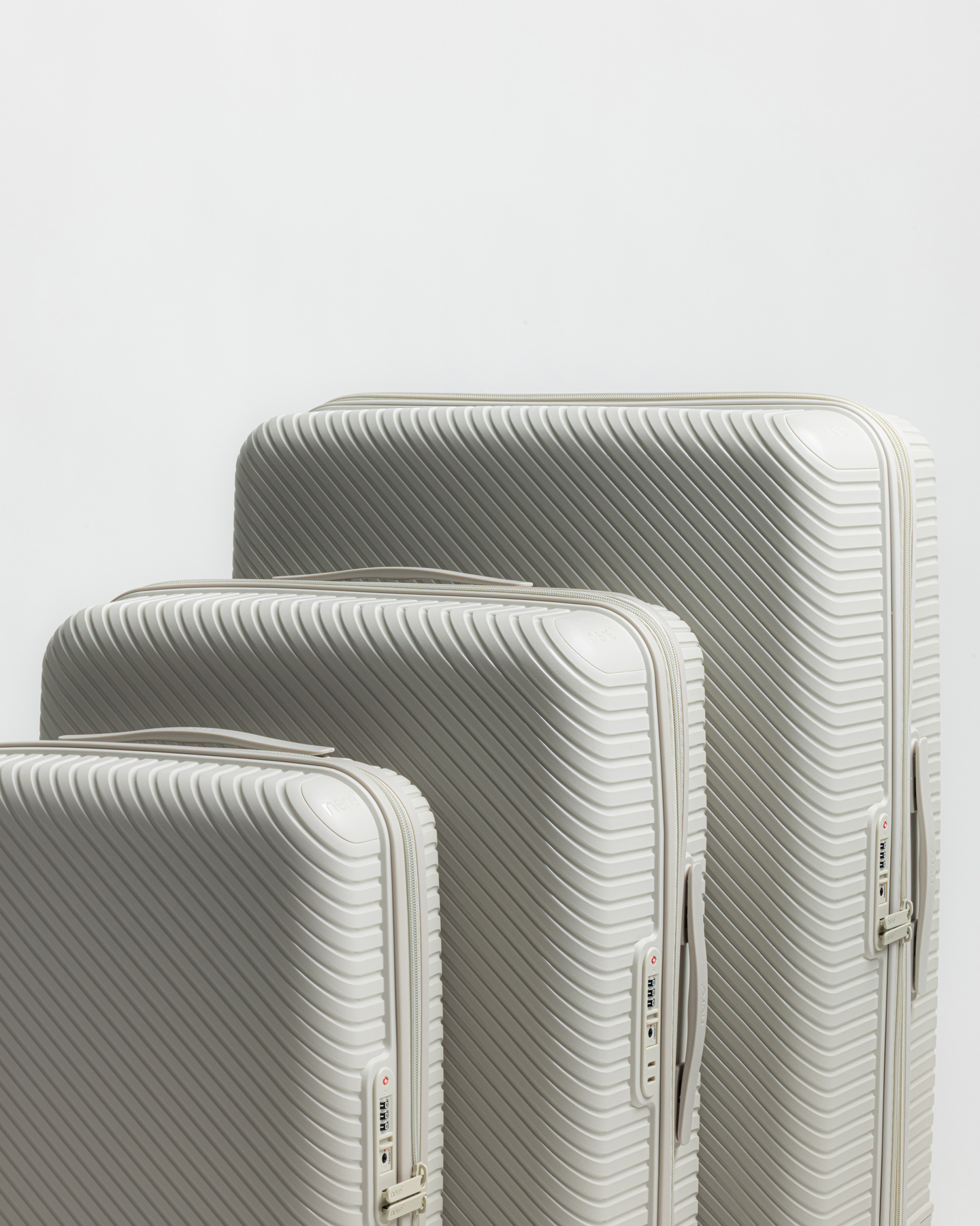Three white hardshell suitcases in different sizes standing side by side