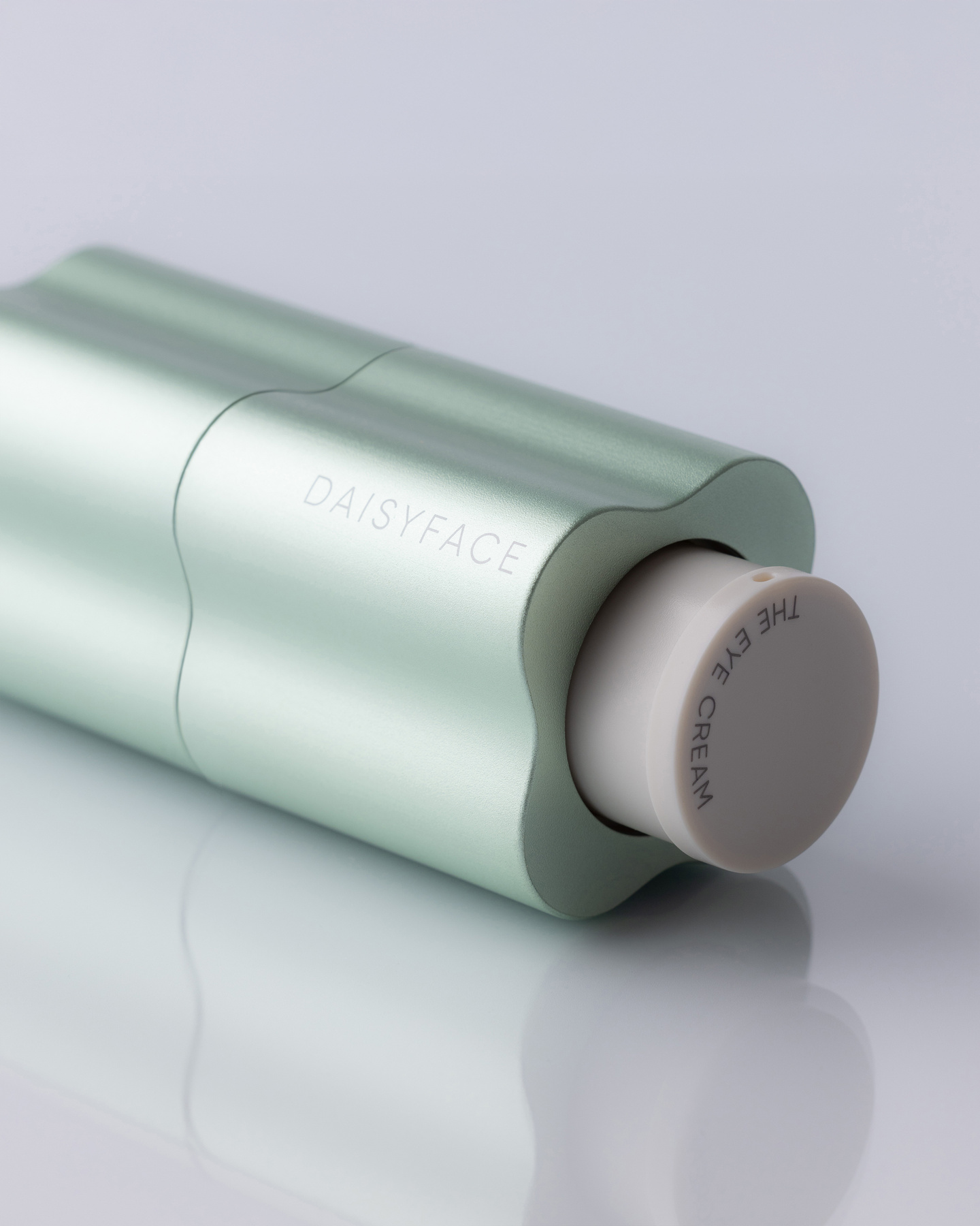 Light green fluted bottle resting at an angle on a reflective surface