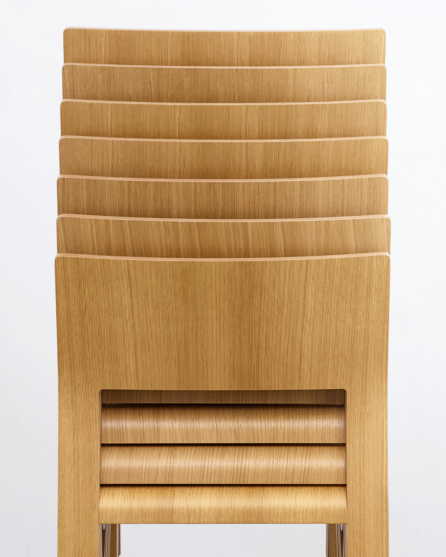 Back view of multiple light wooden chairs stacked vertically to show compact nesting.
