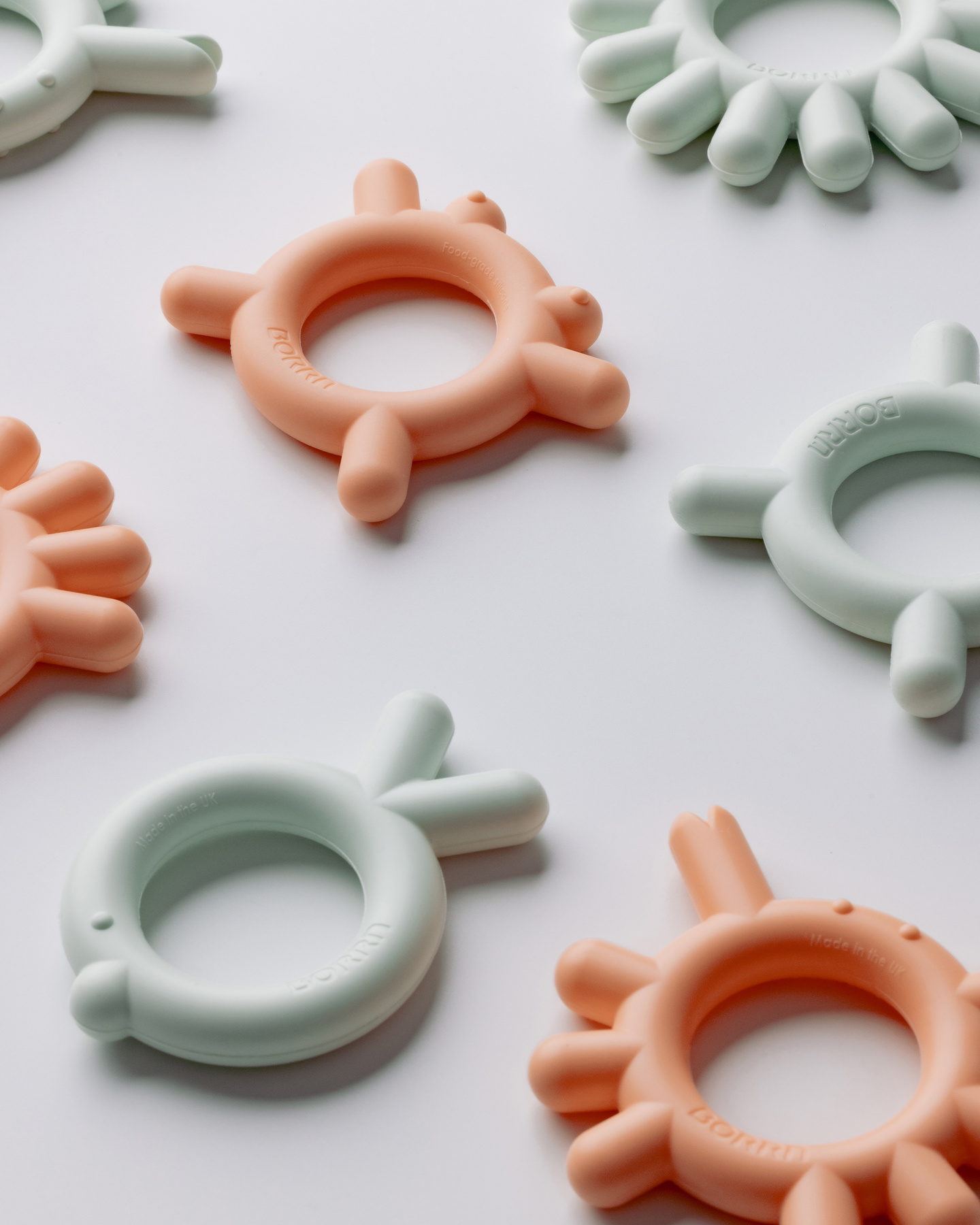 Flat-lay arrangement of pastel peach and green silicone teethers and bottle components.