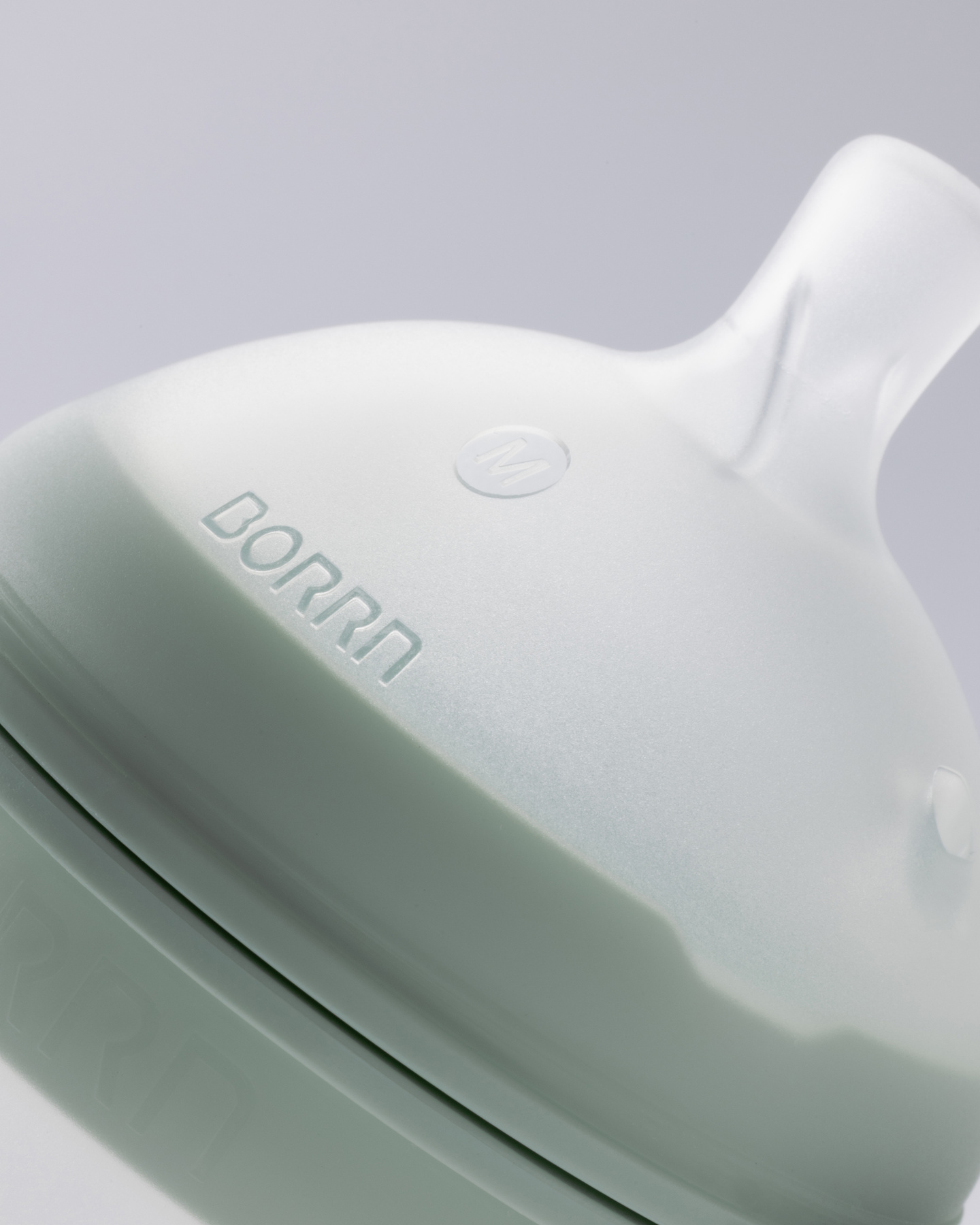 Angled close-up detail of white silicone teat and debossed green collar.
