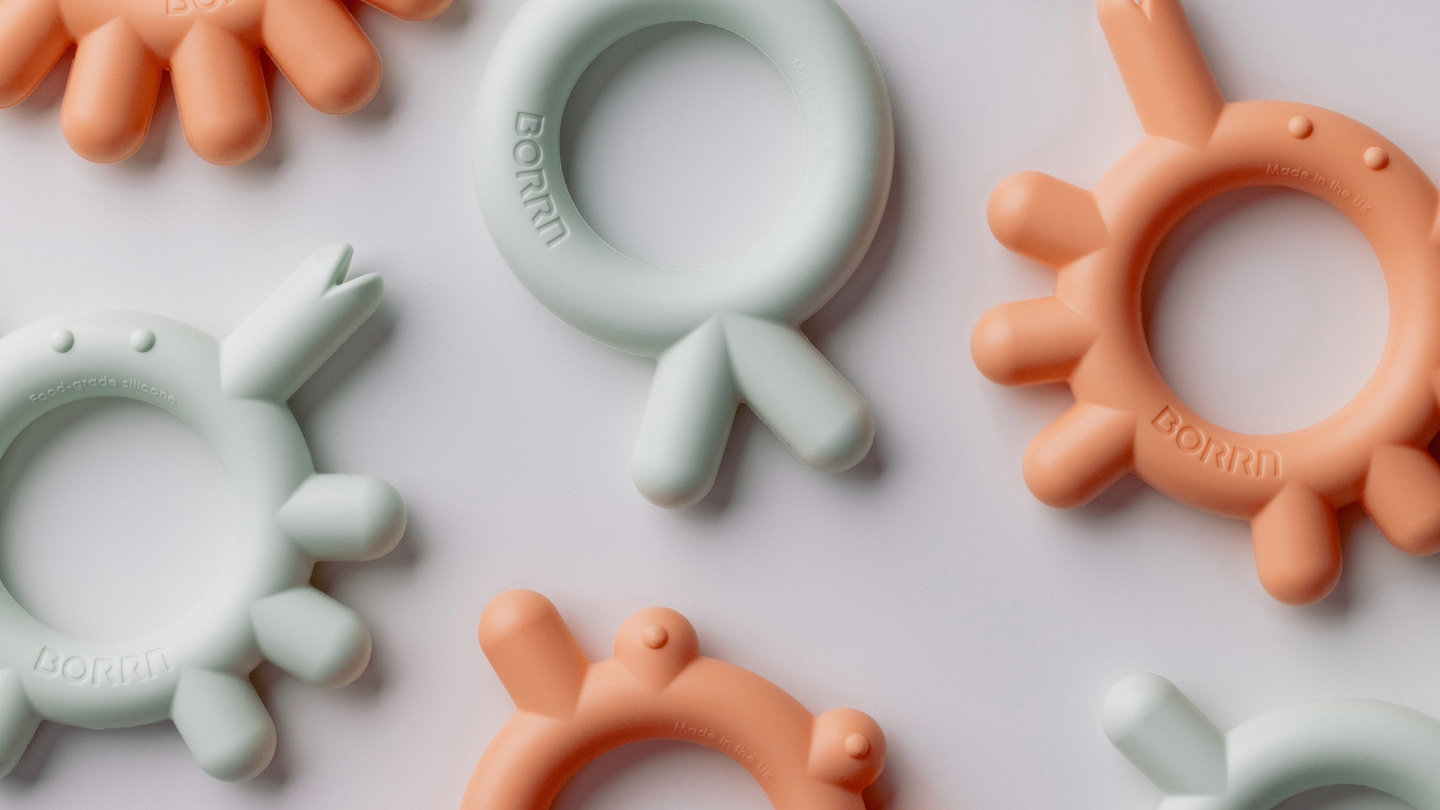 Array of peach and green coloured teethers on a light background.