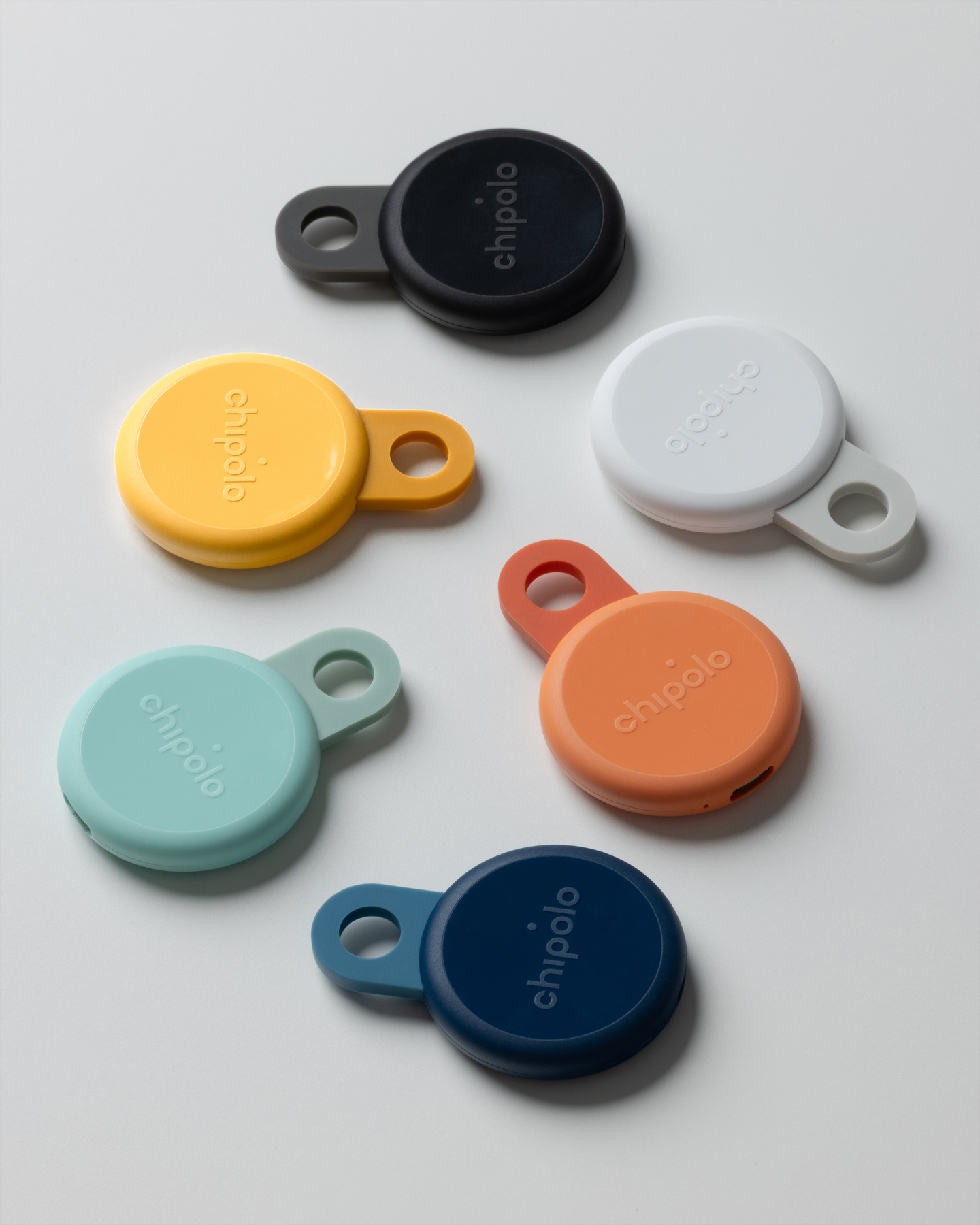 Collection of round Chipolo Loop trackers in multiple colors arranged on a white surface.
