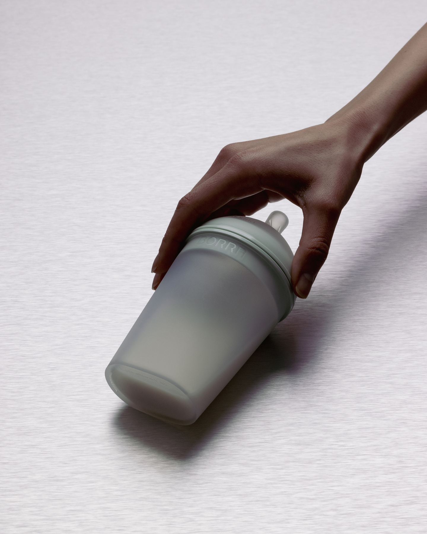 Angled close-up of hand holding translucent silicone baby feeding bottle with milk inside from its top.