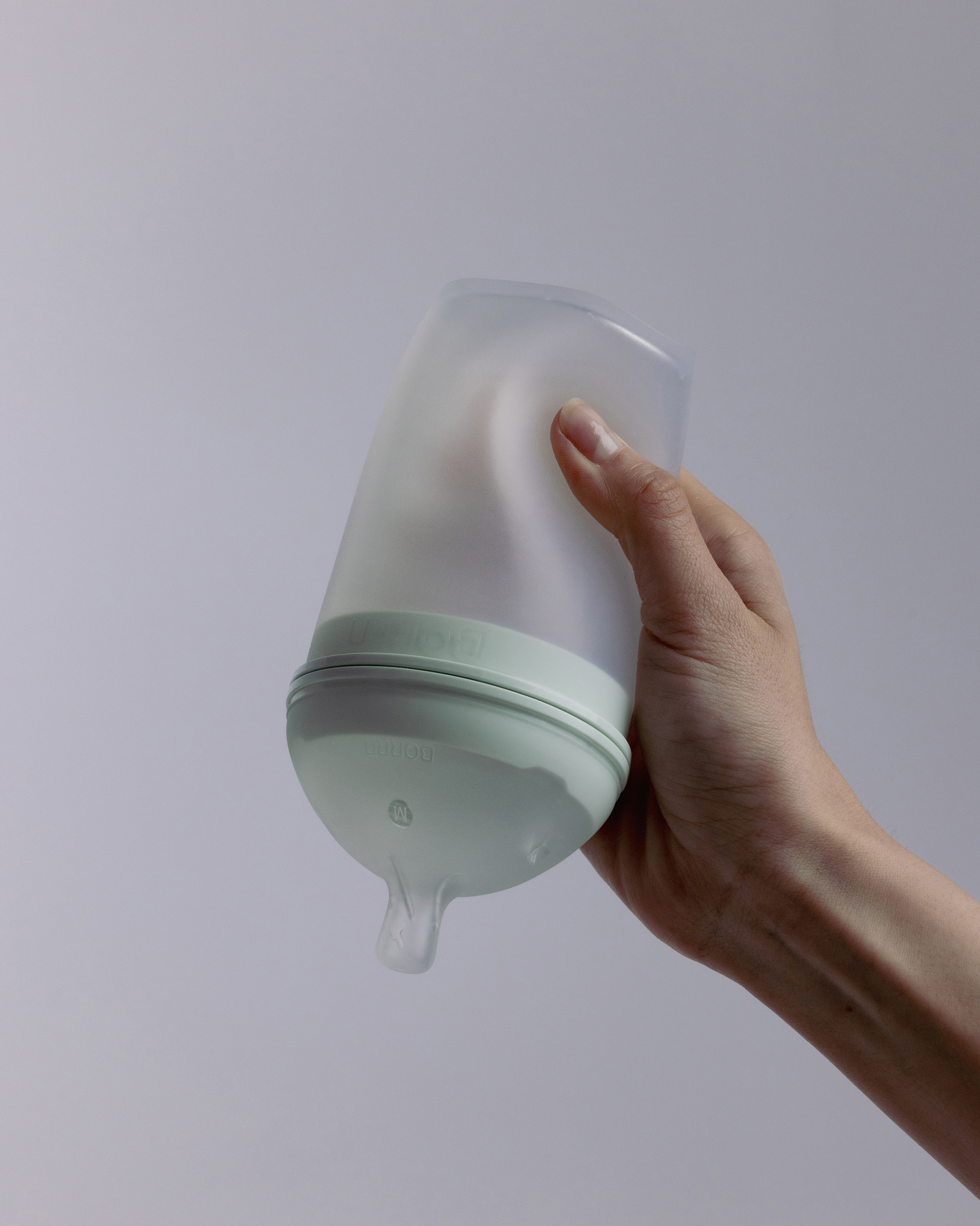 Hand squeezing a flexible translucent silicone baby feeding bottle.