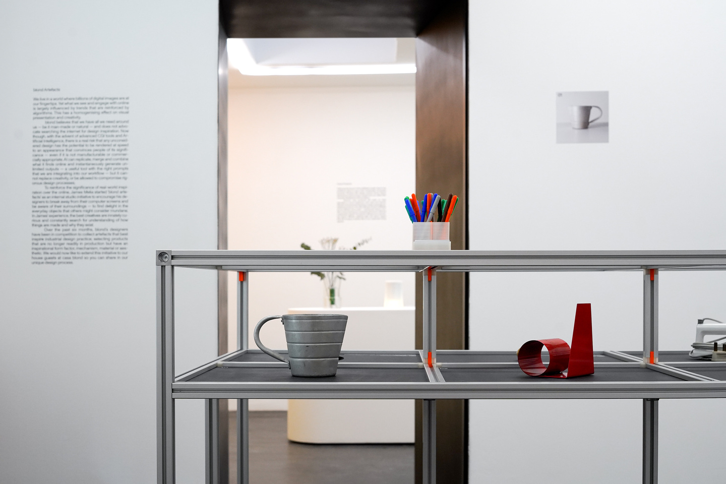 Metal display shelf positioned inside an open doorway in a white gallery space.