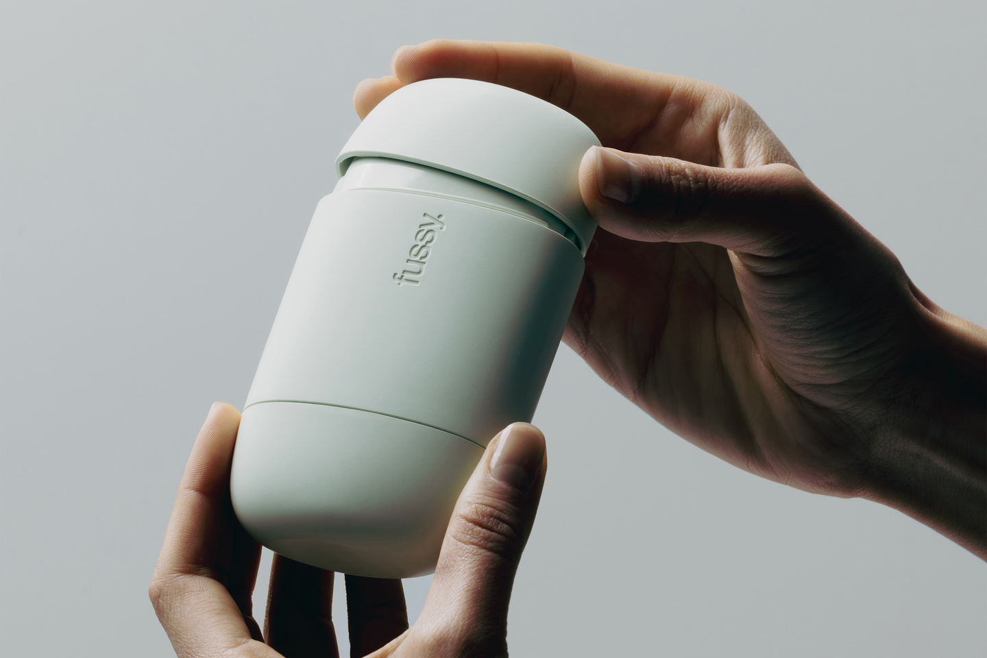 Pair of hands holding a closed mint green Fussy refillable deodorant case.