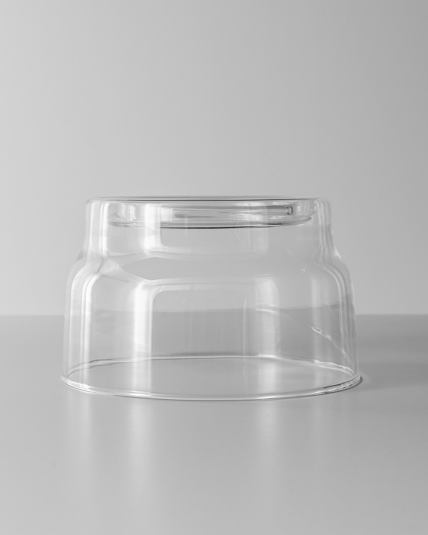 Empty clear glass candle vessel resting on a white surface