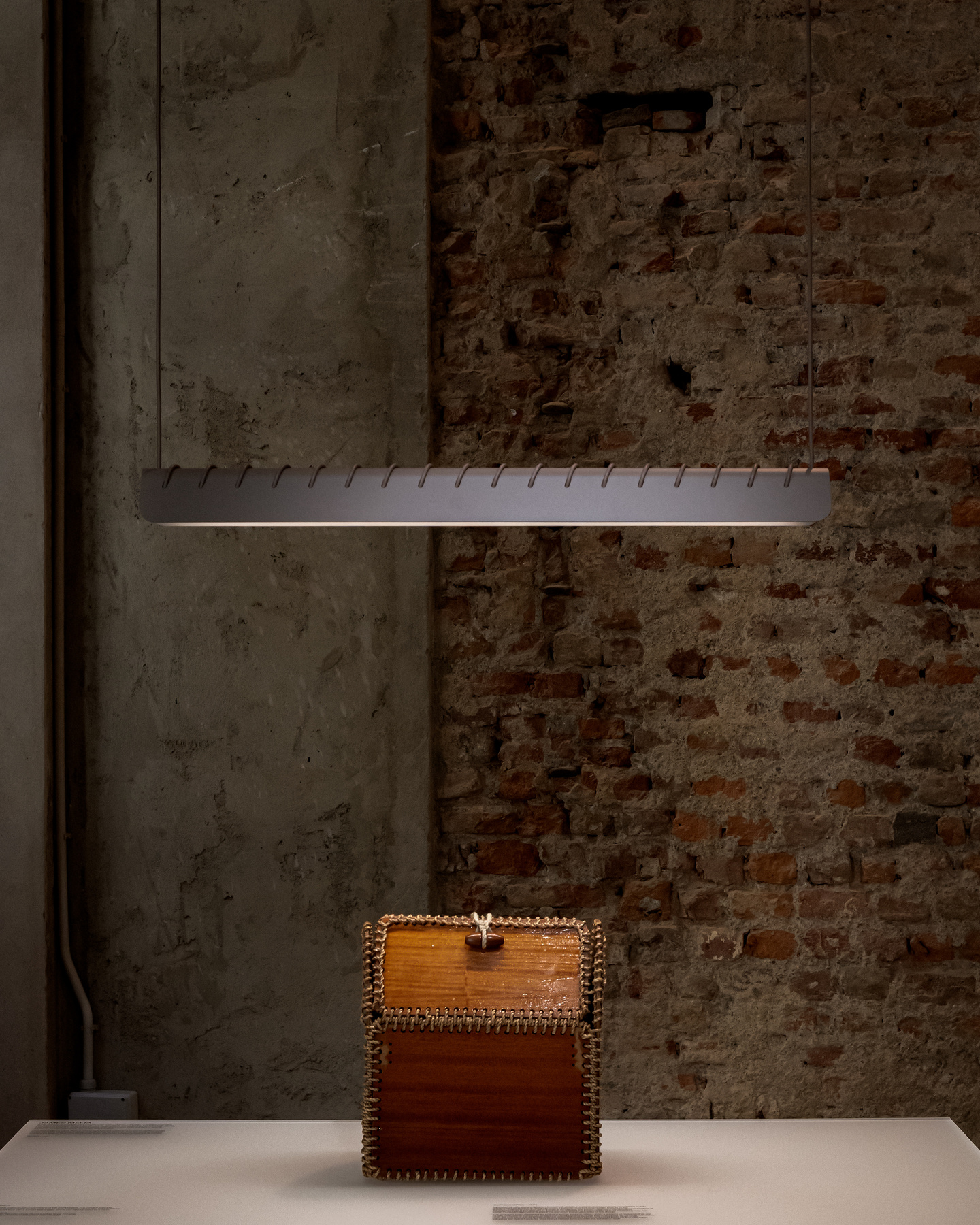 Linear light fixture hanging over wooden cabinet against exposed brick wall