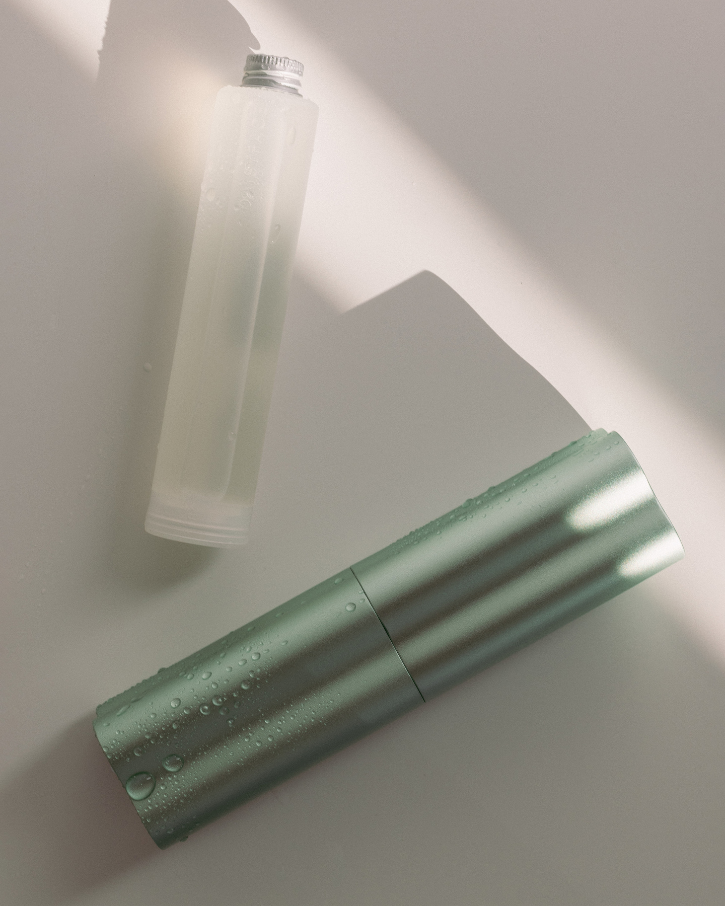 Two green skincare bottles on a light surface with soft sun shadows
