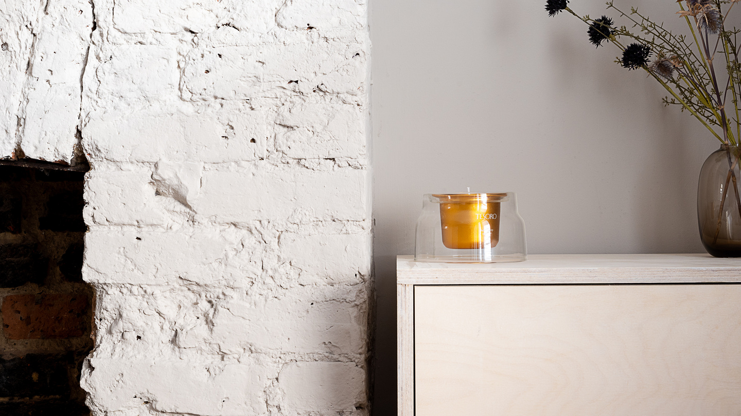 Glass candle vessel with gold insert on a white cabinet in a bright room