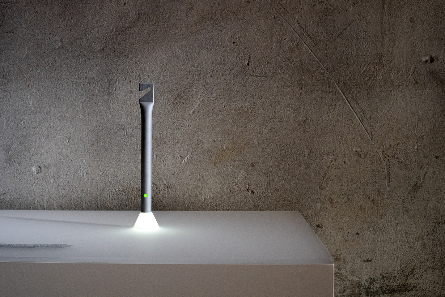 Plinth-standing illuminated vertical light column in front of brick wall