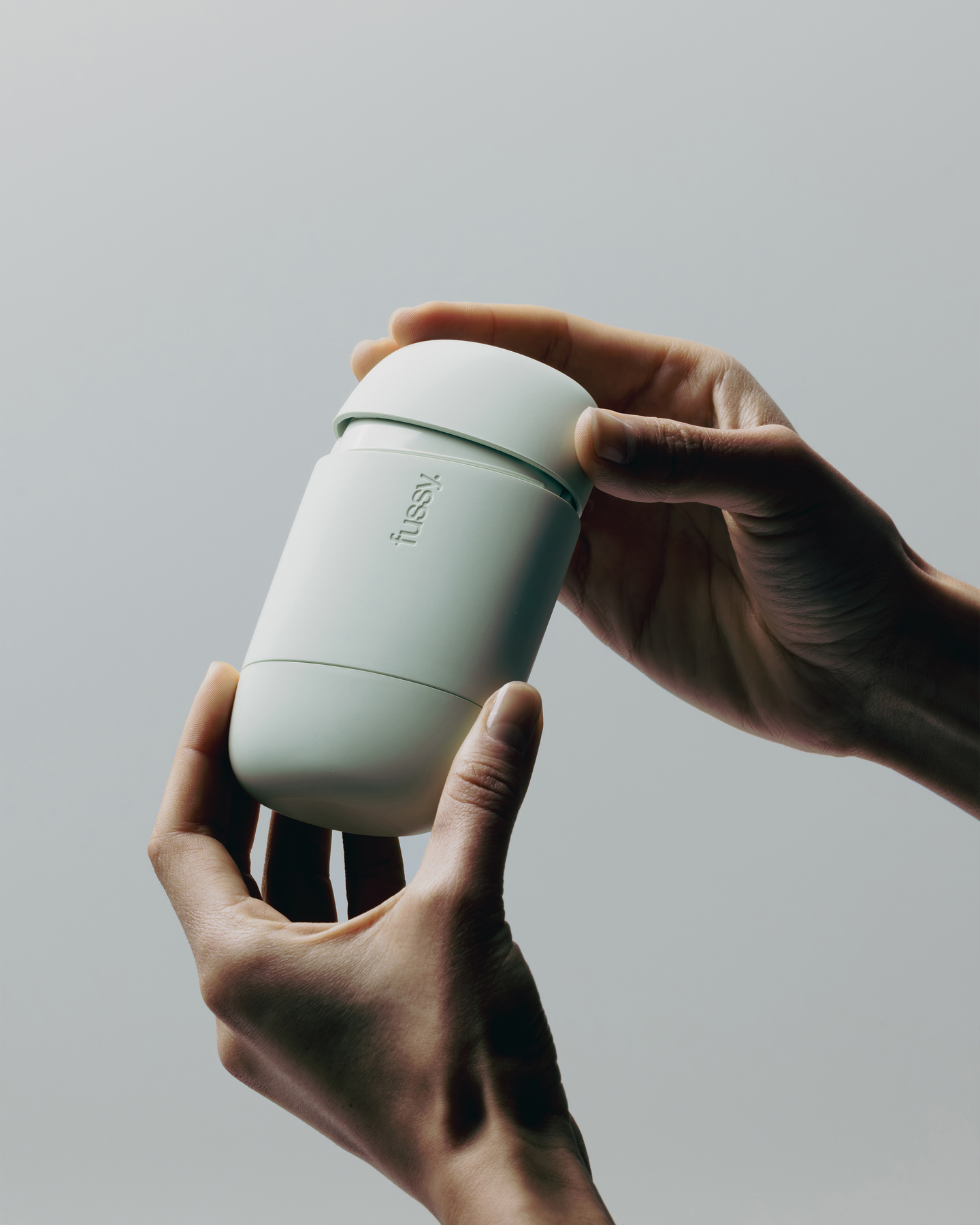 Pair of hands holding a closed mint green Fussy refillable deodorant case.
