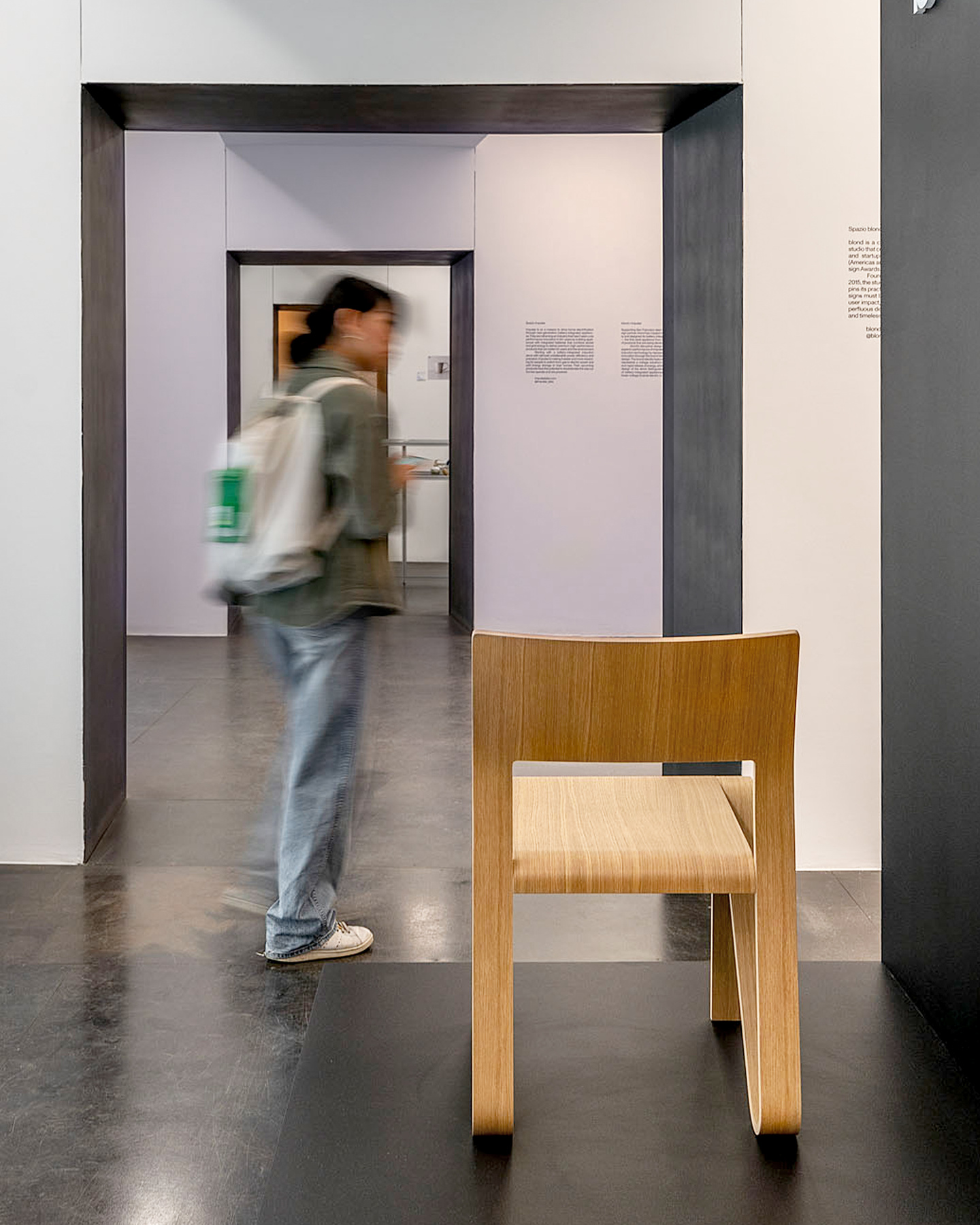 Person walking through an exhibition room past a wooden chair.
