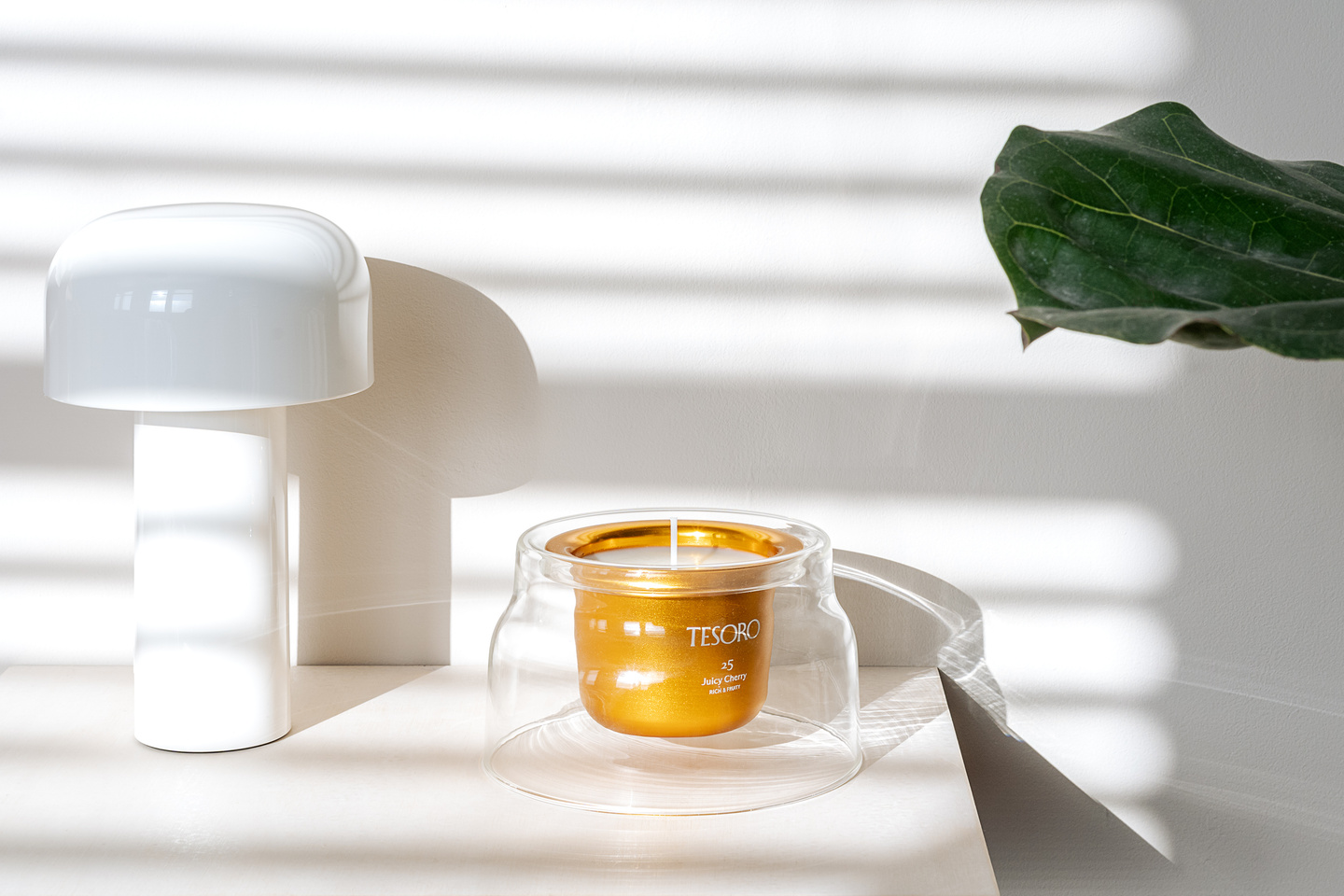 Clear glass candle vessel with gold insert displayed on a white shelf