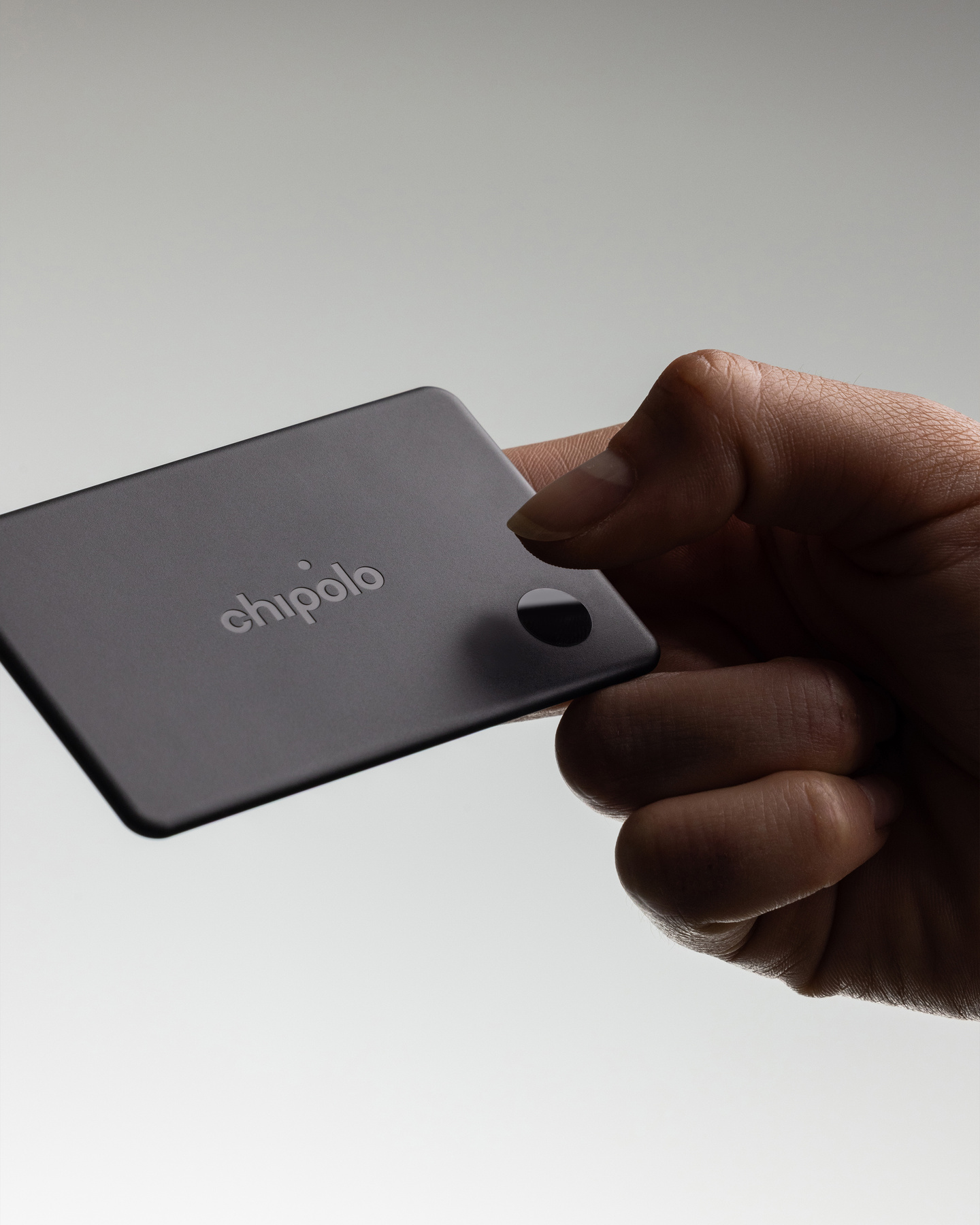 Hand holding a thin dark Chipolo Card tracker between fingers.