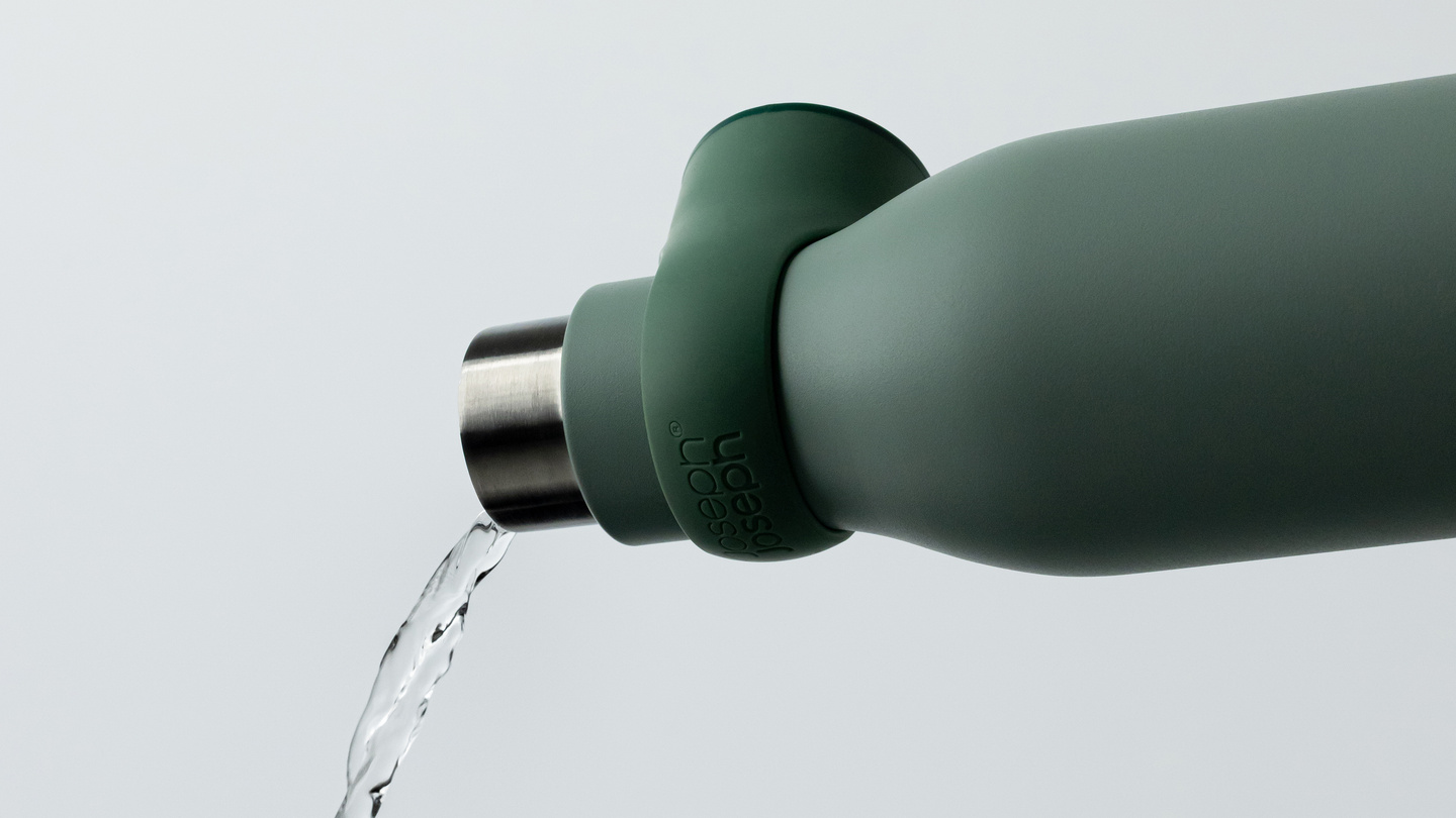 Water pouring from a green water bottle against a neutral background