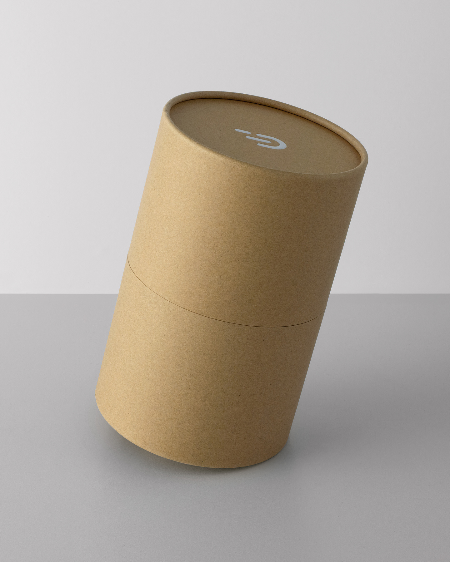 View of closed cylindrical cardboard packaging container balancing on it's edge on a grey surface.