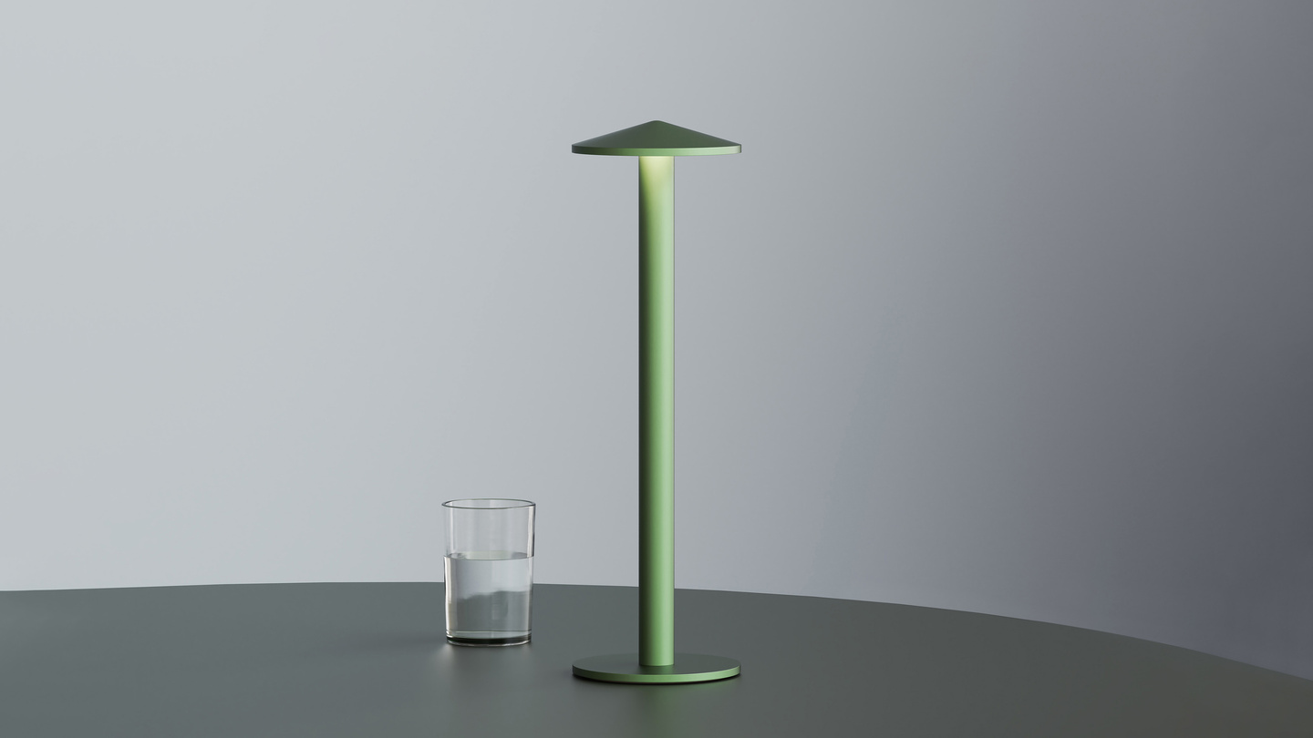 Green Parasol Lamp standing next to a water glass on a table.