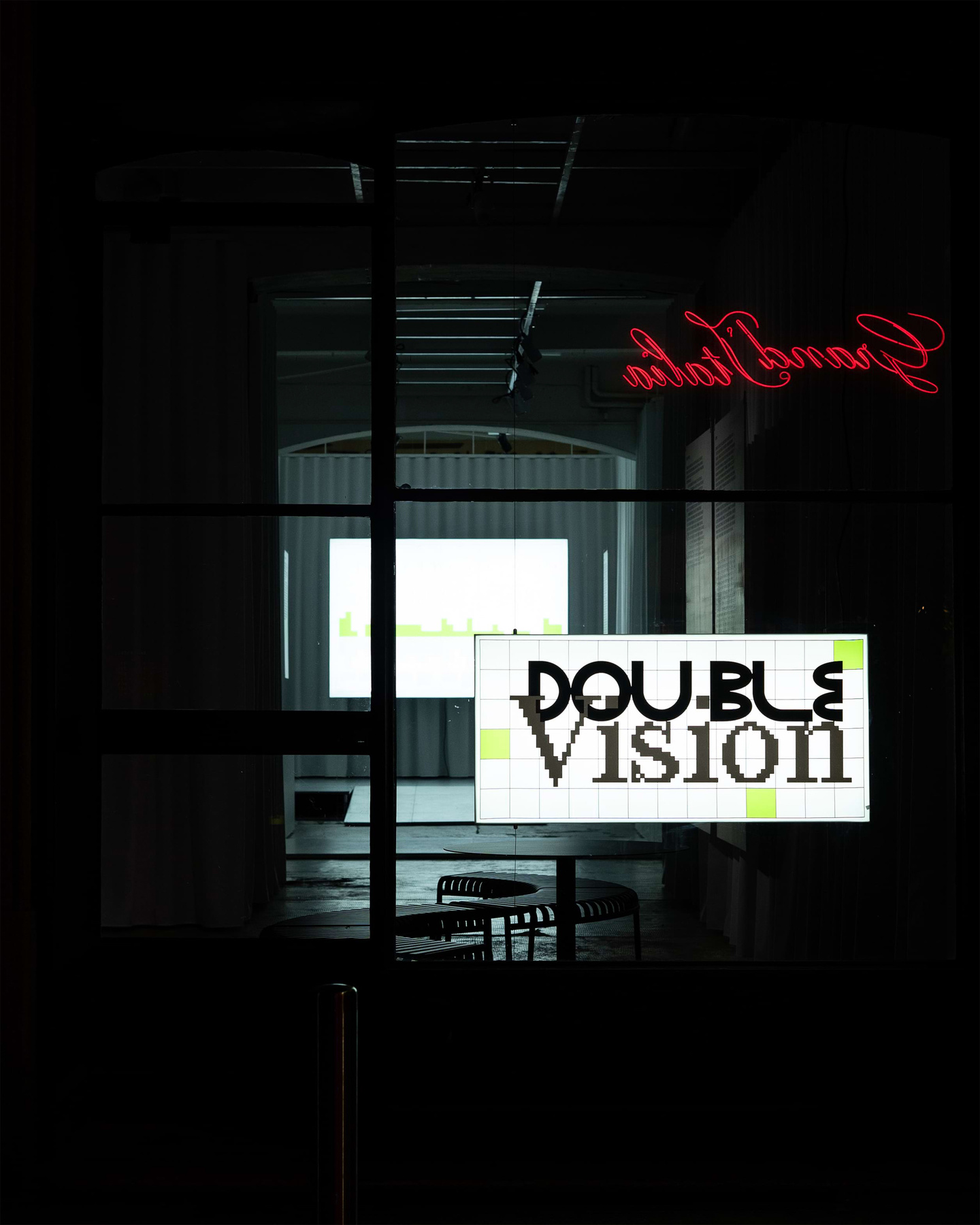 Double Vision graphic branding displayed on a glass window at night