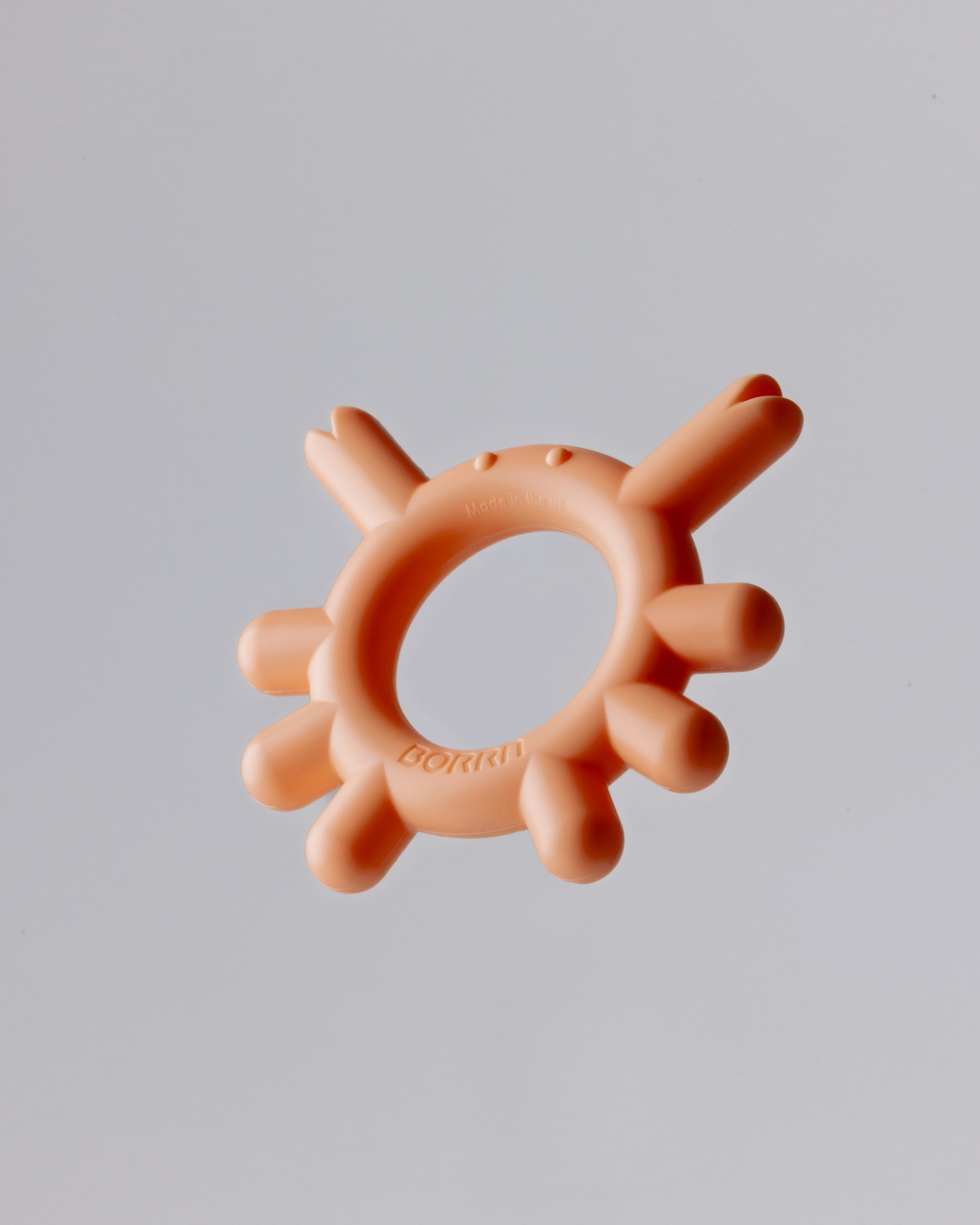 Peach-coloured circular silicone teether ring shown on a light background.