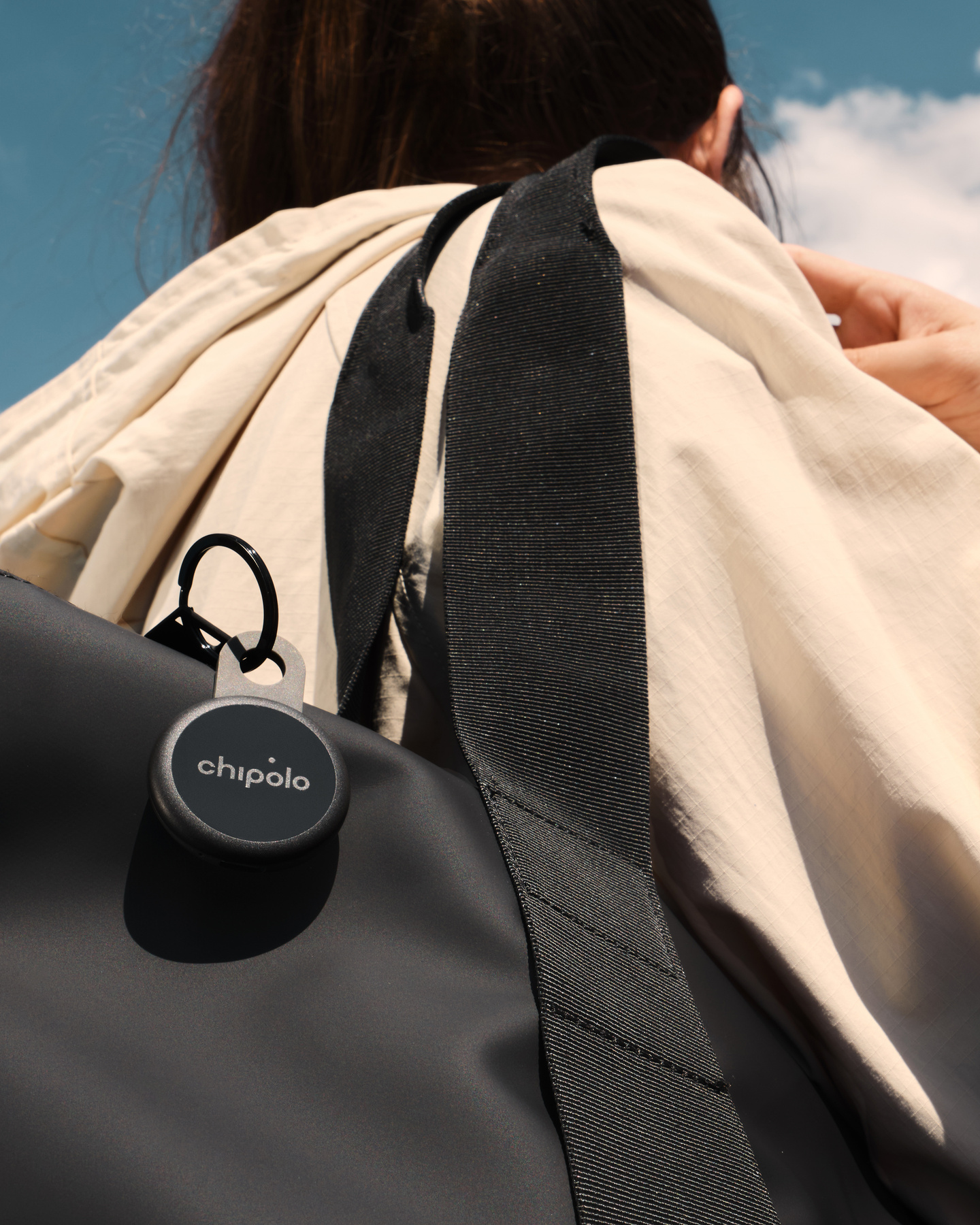 Person wearing a black backpack with a black Chipolo tracker attached to the strap.
