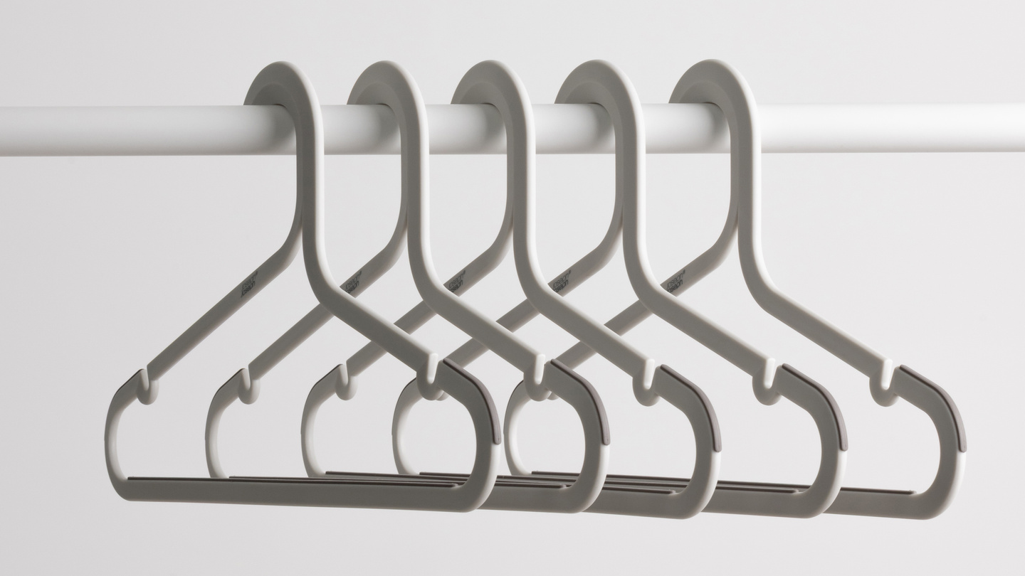 Row of five grey coat hangers with trouser hooks resting on a rail