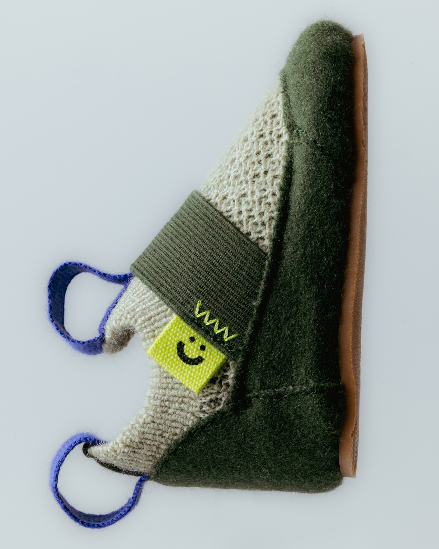 Studio shot showing the side profile of a green knitted children's shoe.