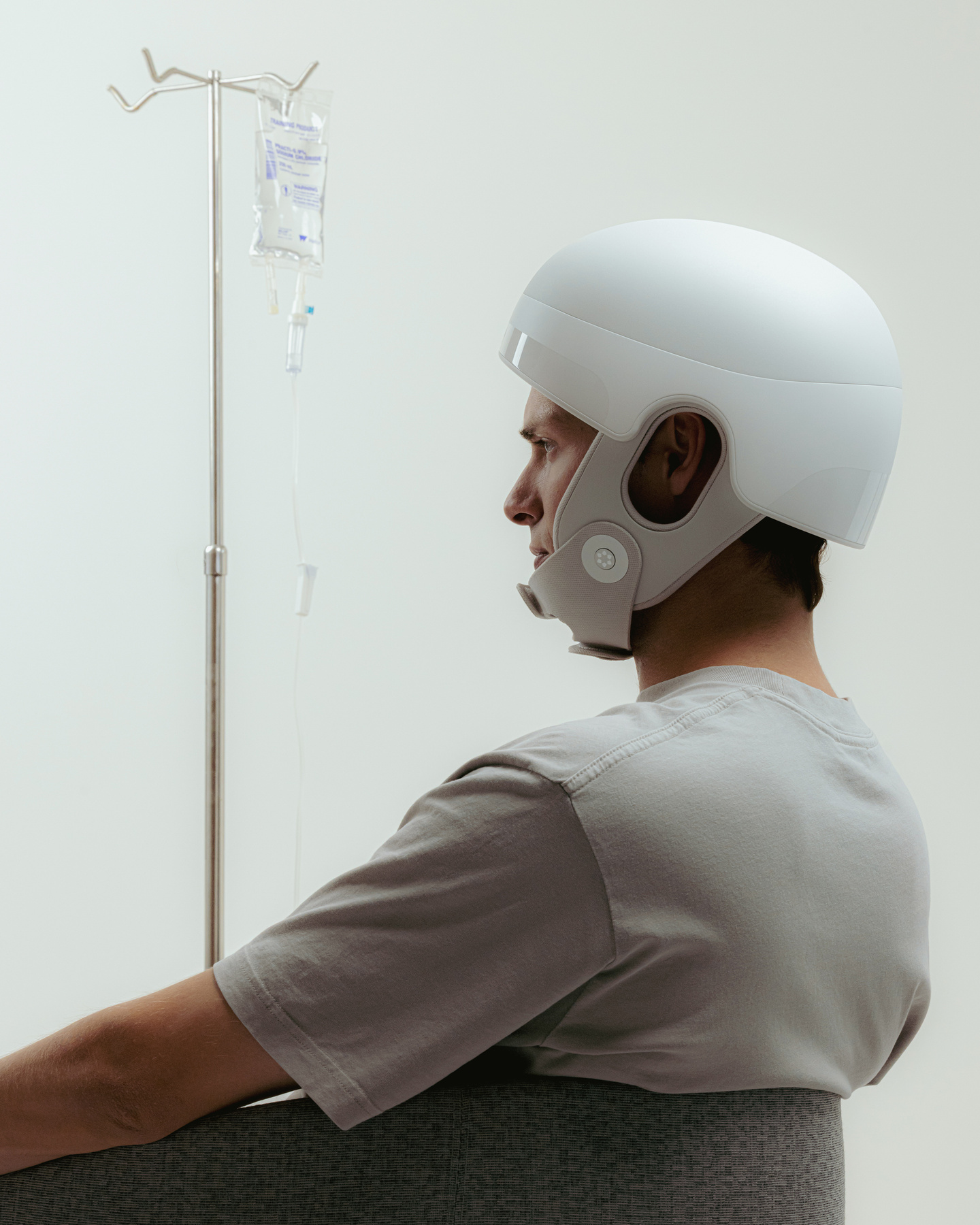 Man sitting in profile wearing a white medical helmet device near a medical pole