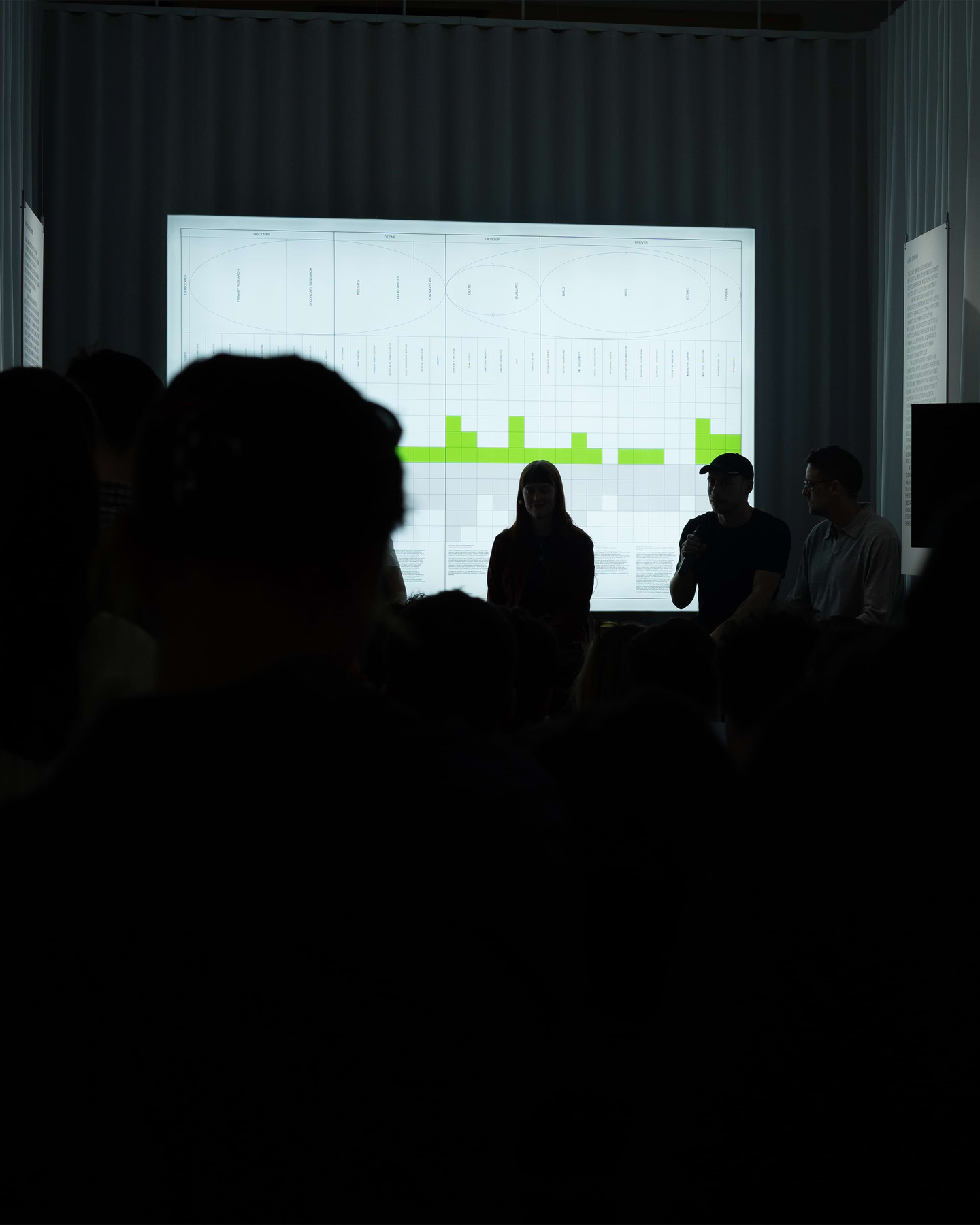 Silhouetted event attendees standing in a dark room watching a presentation screen